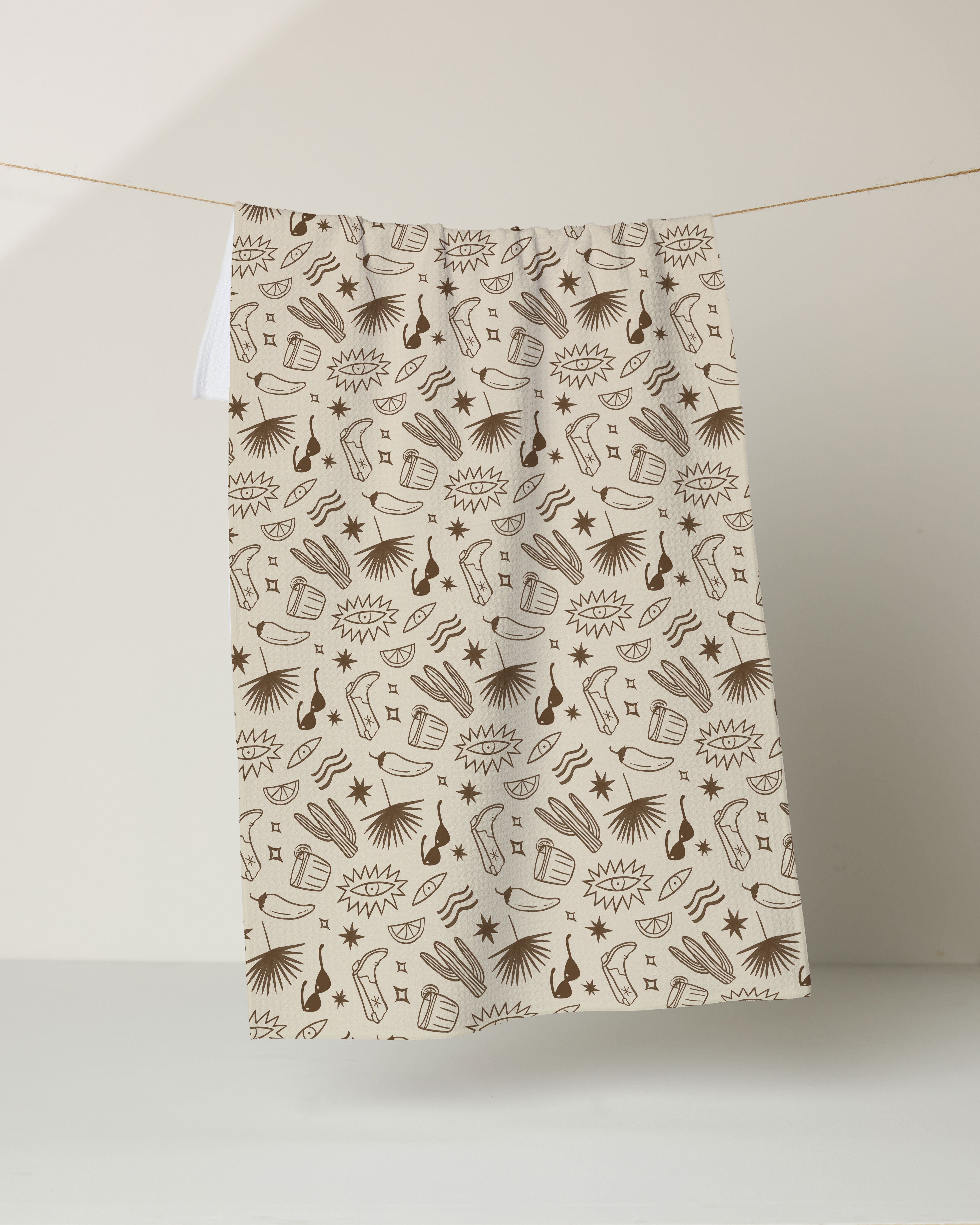 The Bonfire Nights tea towel by Geometry features brown, hand-drawn style musical instruments, books, and abstract shapes on beige. Made from recycled materials, it hangs against a light background.