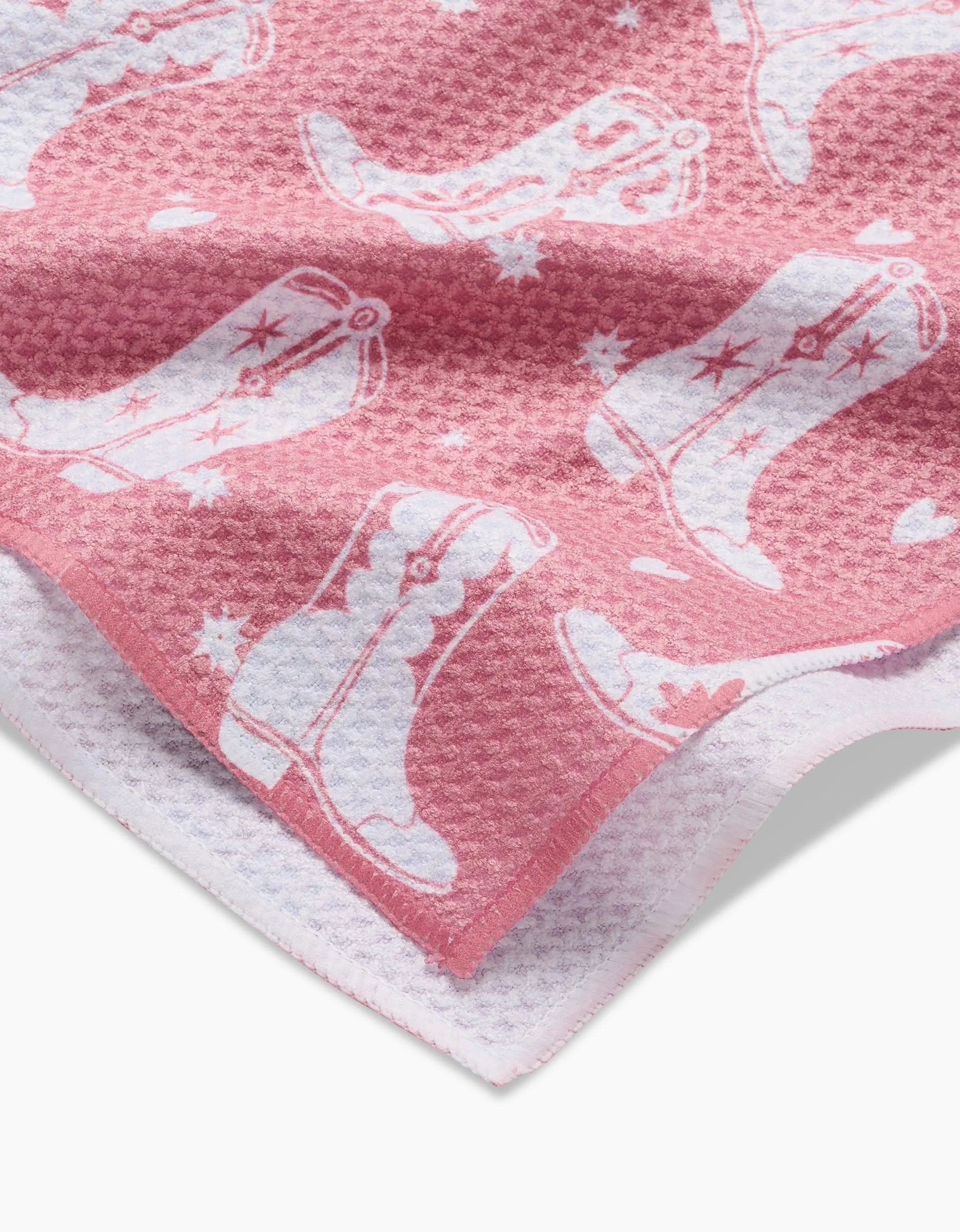 The Boots On Worries Gone tea towel by Aubrey Fairchild features pink textured Geoweave fabric with white cowboy boots and stars, a folded corner showing the white underside, and is crafted from recycled materials for eco-friendly appeal.