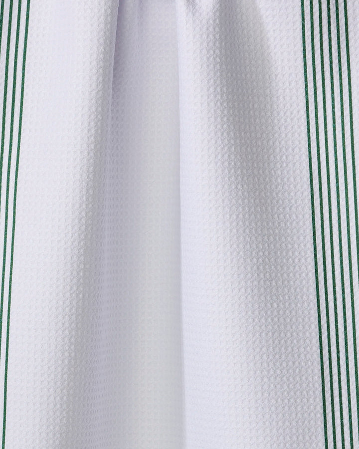A close-up of The Buy Guide’s Borderline - Evergreen kitchen tea towel, featuring white textured fabric with vertical green stripes along the edges, crafted from recycled materials.