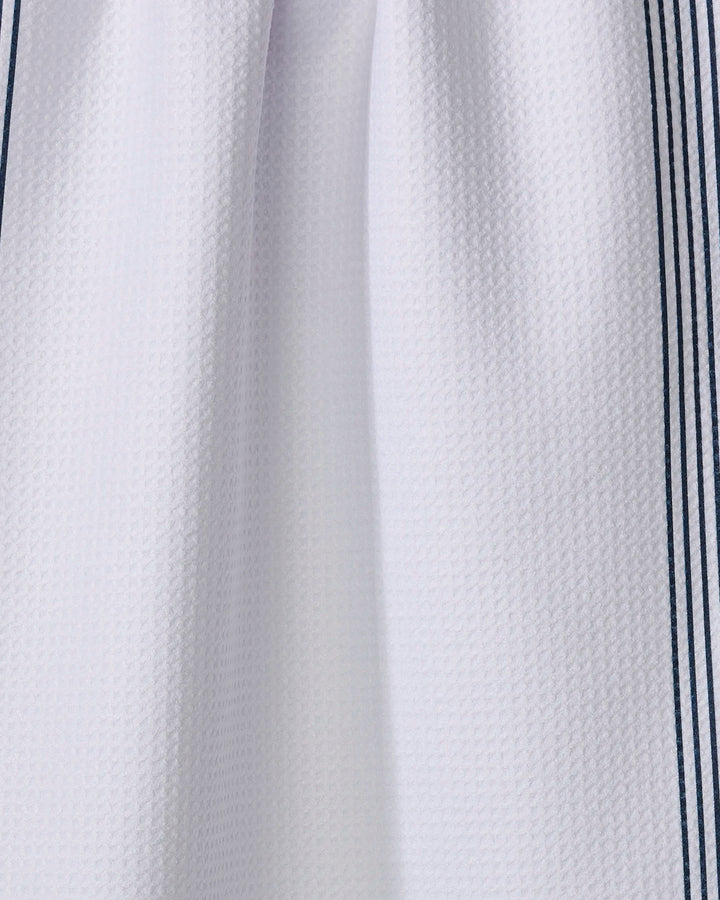 Close-up of The Buy Guide’s Borderline - Navy towel, featuring a white waffle-textured fabric with two thin navy stripes on each side. Made from recycled materials, the ultra-absorbent towel is slightly gathered at the top center.