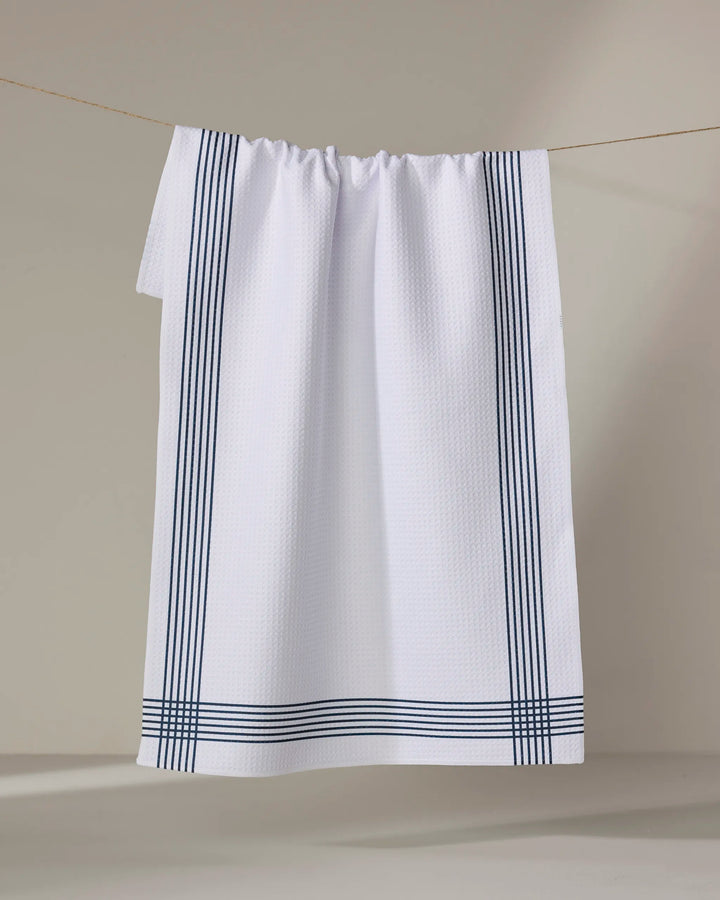 The Buy Guide's Borderline - Navy tea towel hangs on a line, featuring a textured white design with three parallel navy stripes along the edges against a neutral background.