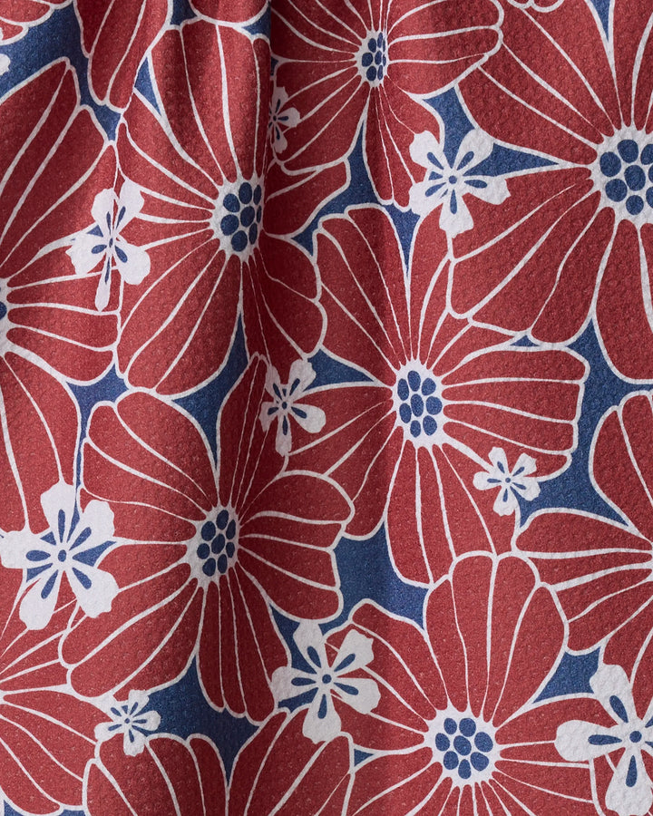 A close-up of the Ashley Celena "Botanical Blush" tea towel—ultra-absorbent, made from recycled materials, with large red flowers, blue centers, white outlines, small white blooms, all on a blue background.