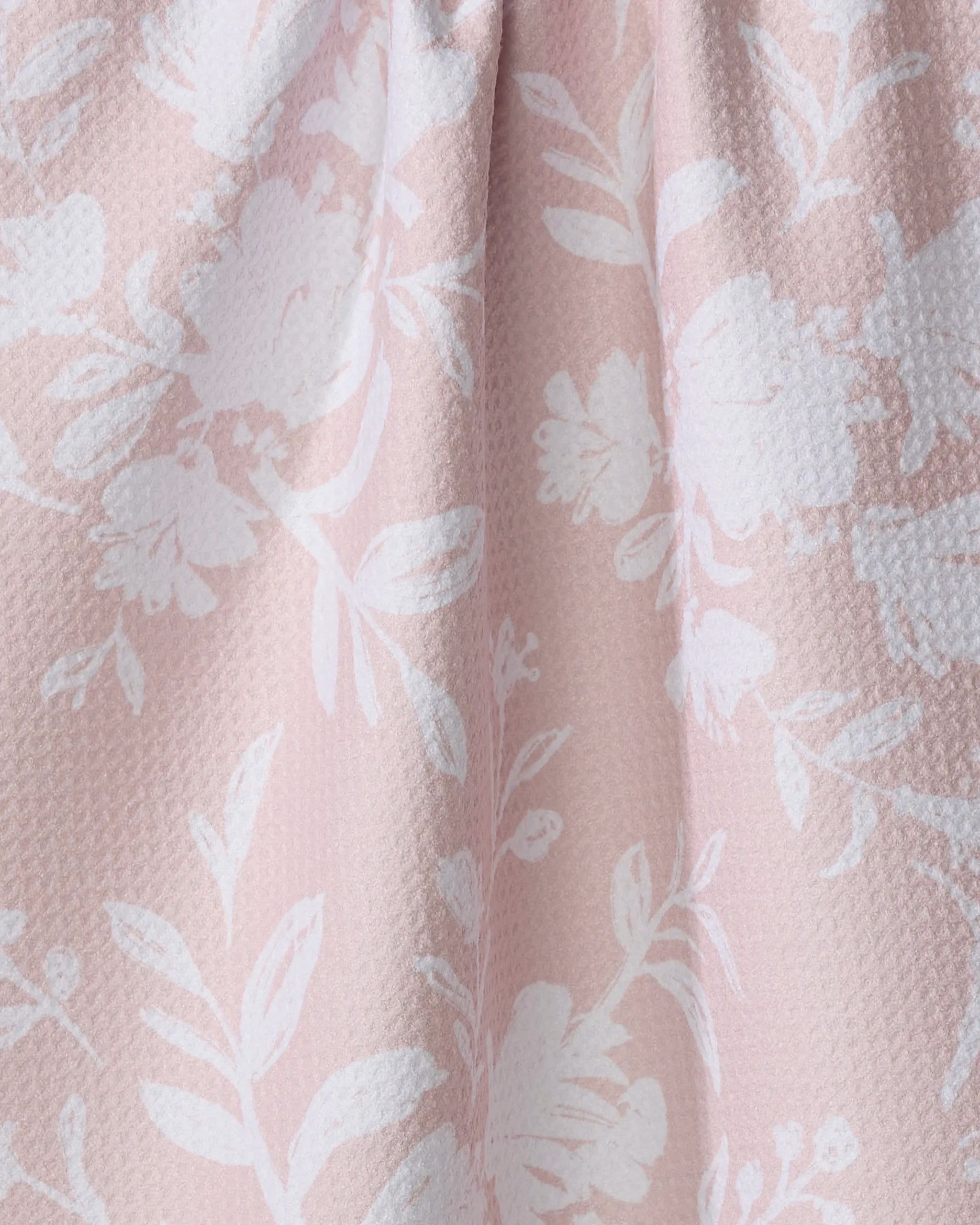 Close-up of Danelys Sidron's Botanical Silhouettes Blush—a light pink fabric with a textured surface, featuring white floral and leaf patterns. Made from recycled materials, its gentle folds create soft shadows and highlights.