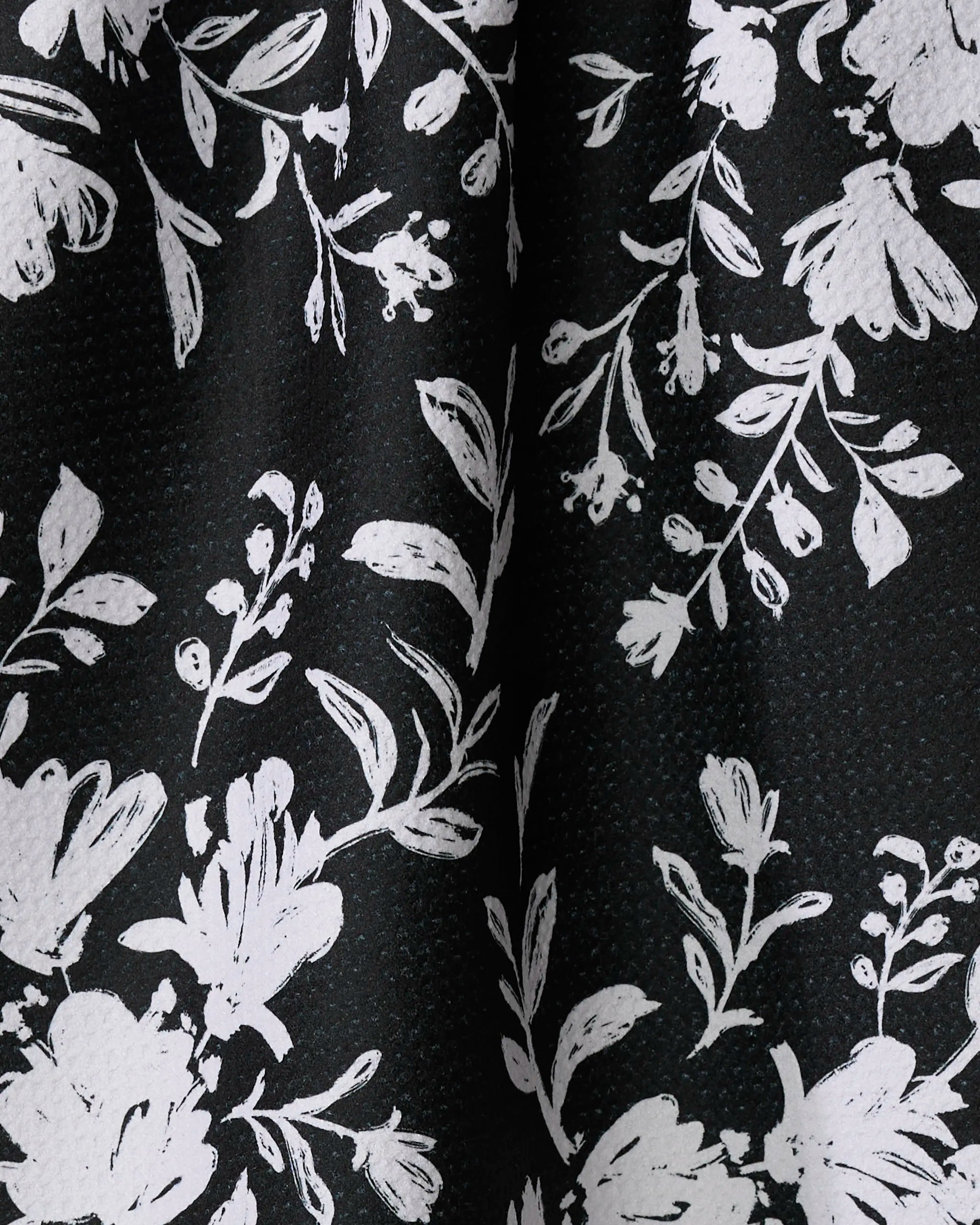 Botanical Silhouettes Charcoal by Danelys Sidron features white floral and leaf patterns on a black textured background—ideal for a stylish, recycled-material tea towel.