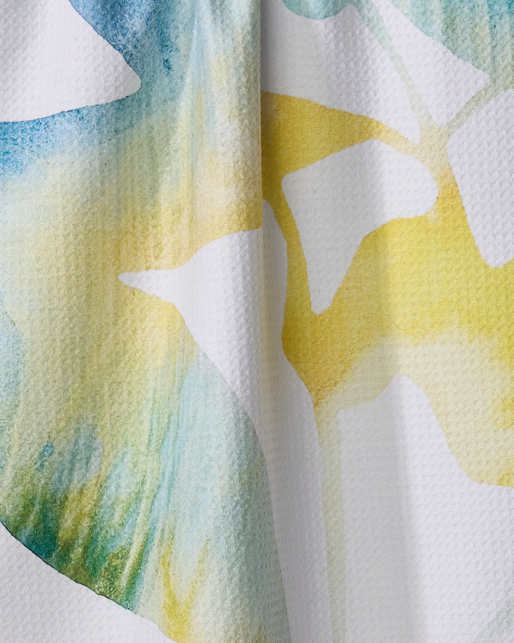 Close-up of Rachel Austin’s "Botanical Watercolor Dews" ultra-absorbent white tea towel, adorned with blue, green, and yellow abstract watercolor patterns and a subtle vertical fold.