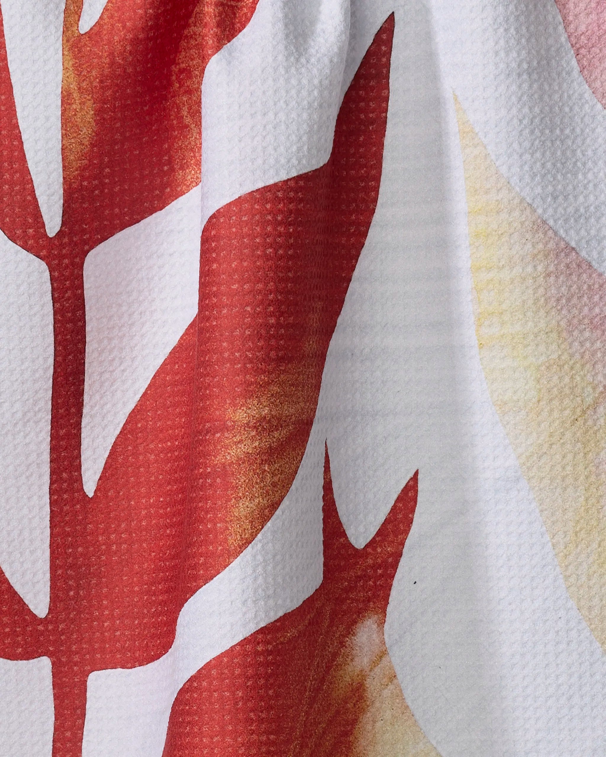 Close-up of Rachel Austin’s Botanical Watercolor Light tea towel, showcasing a textured surface and bold red-orange leaf pattern with yellow gradients on white. Eco-friendly, crafted from recycled materials.