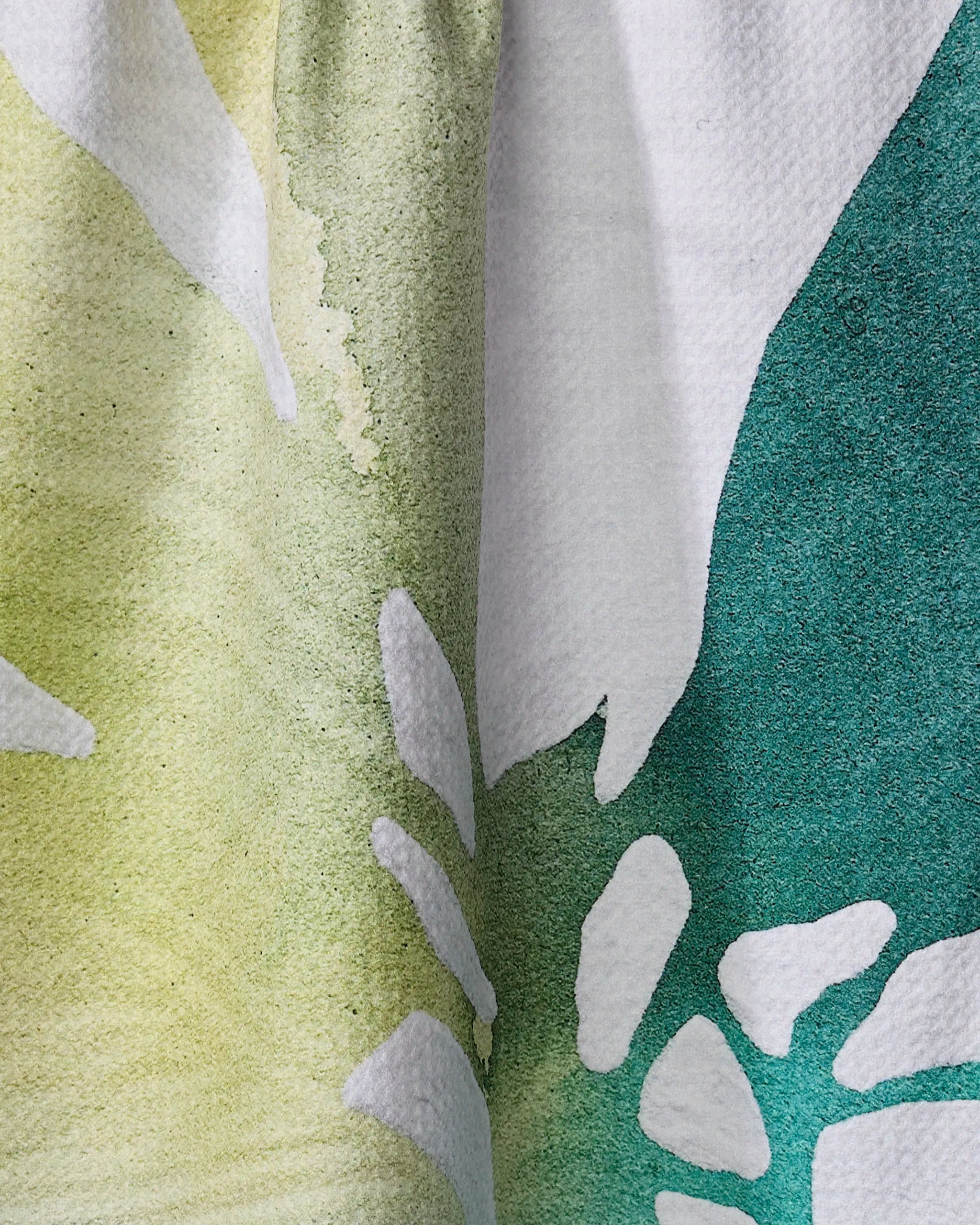 Close-up of Rachel Austin's "Botanical Watercolor Sea" tea towel, showcasing a vibrant yellow, white, and green pattern with petal-like shapes. The textured fabric is quick-drying and made from recycled materials.