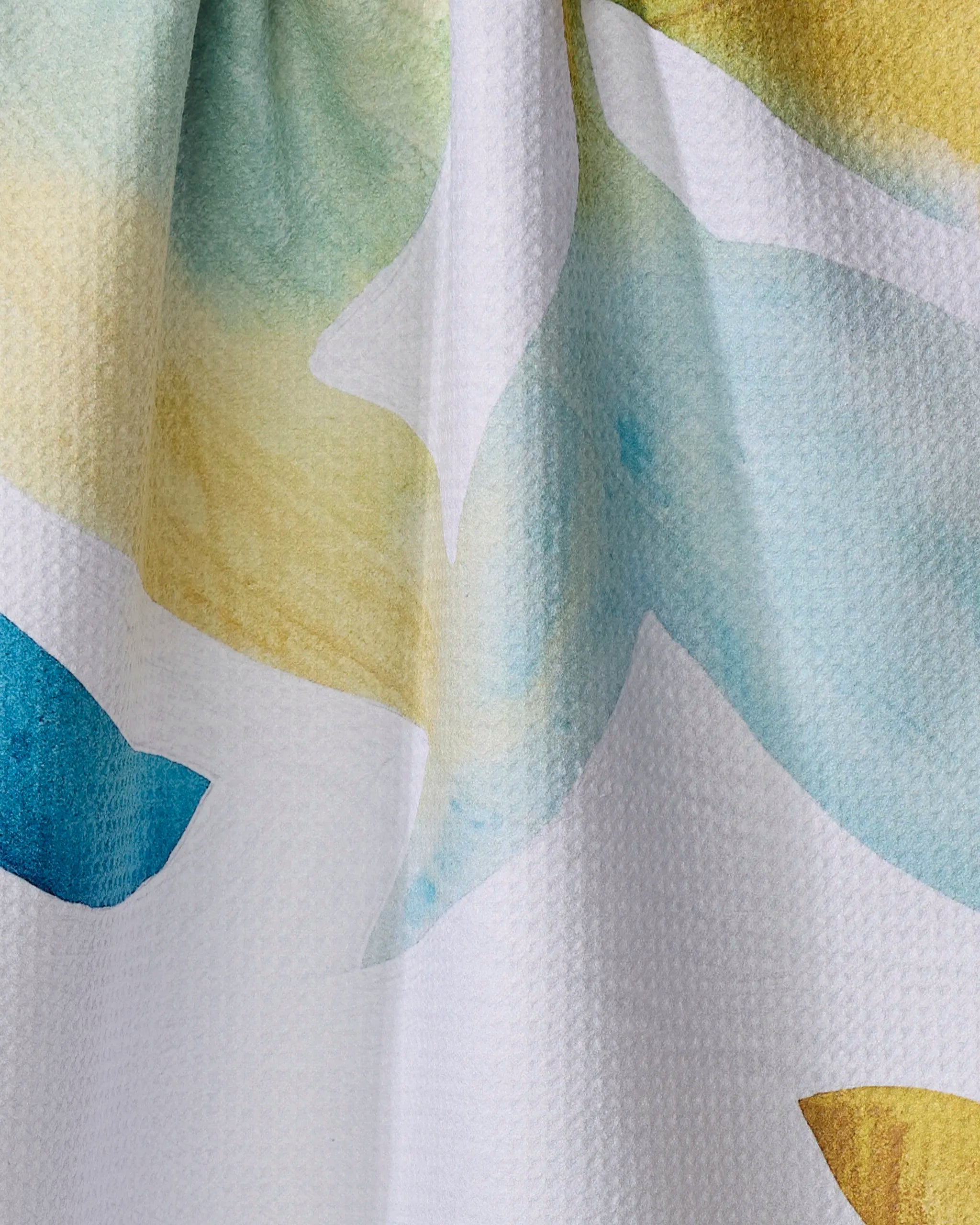 A close-up of Rachel Austin's "Botanical Watercolor Spring" recycled kitchen towel, showcasing white textured fabric with blue, yellow, and green abstract watercolor patterns.