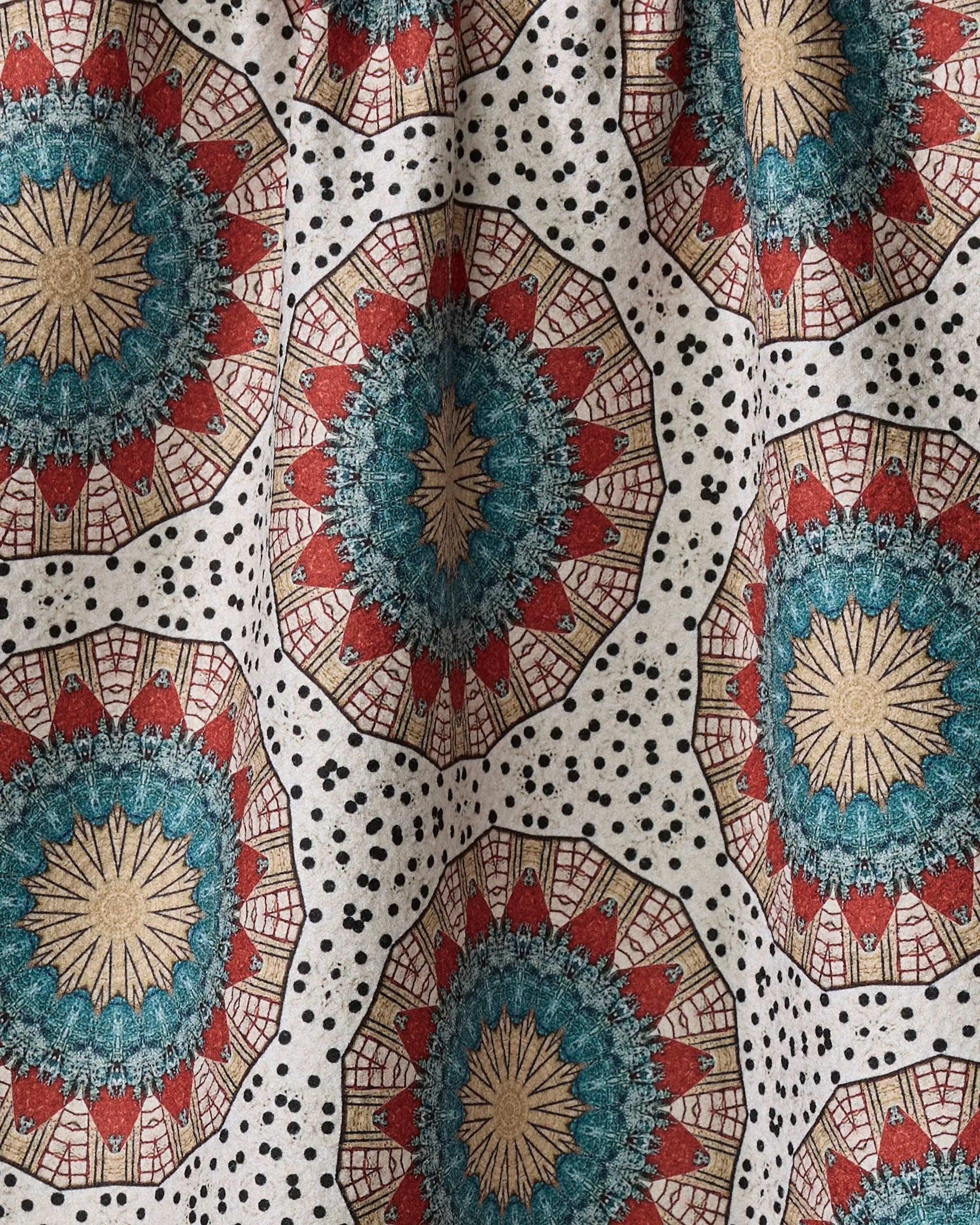 The Katherine Berkeley "Bottle Cap Boogie Woogie" towel features large teal, red, and beige circular mandalas with small black dots on white. Its quick-drying fabric is slightly gathered, displaying natural folds and shadows.