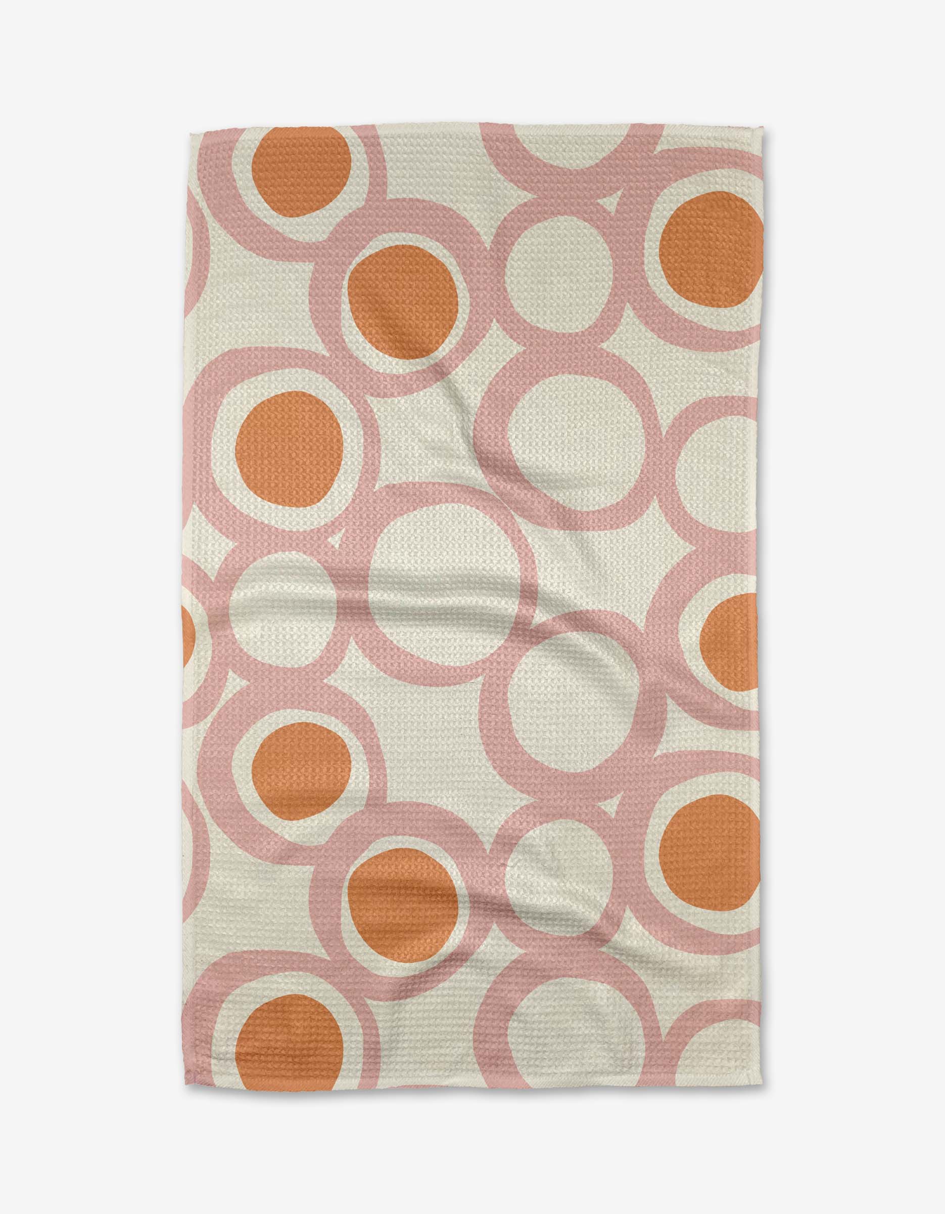 The Lizzie Clark Bouncing Balls Tea Towel features large, overlapping pink circles with orange centers on a cream background. Made from Geoweave fabric, this rectangular tea towel lies flat with a slightly wrinkled look.