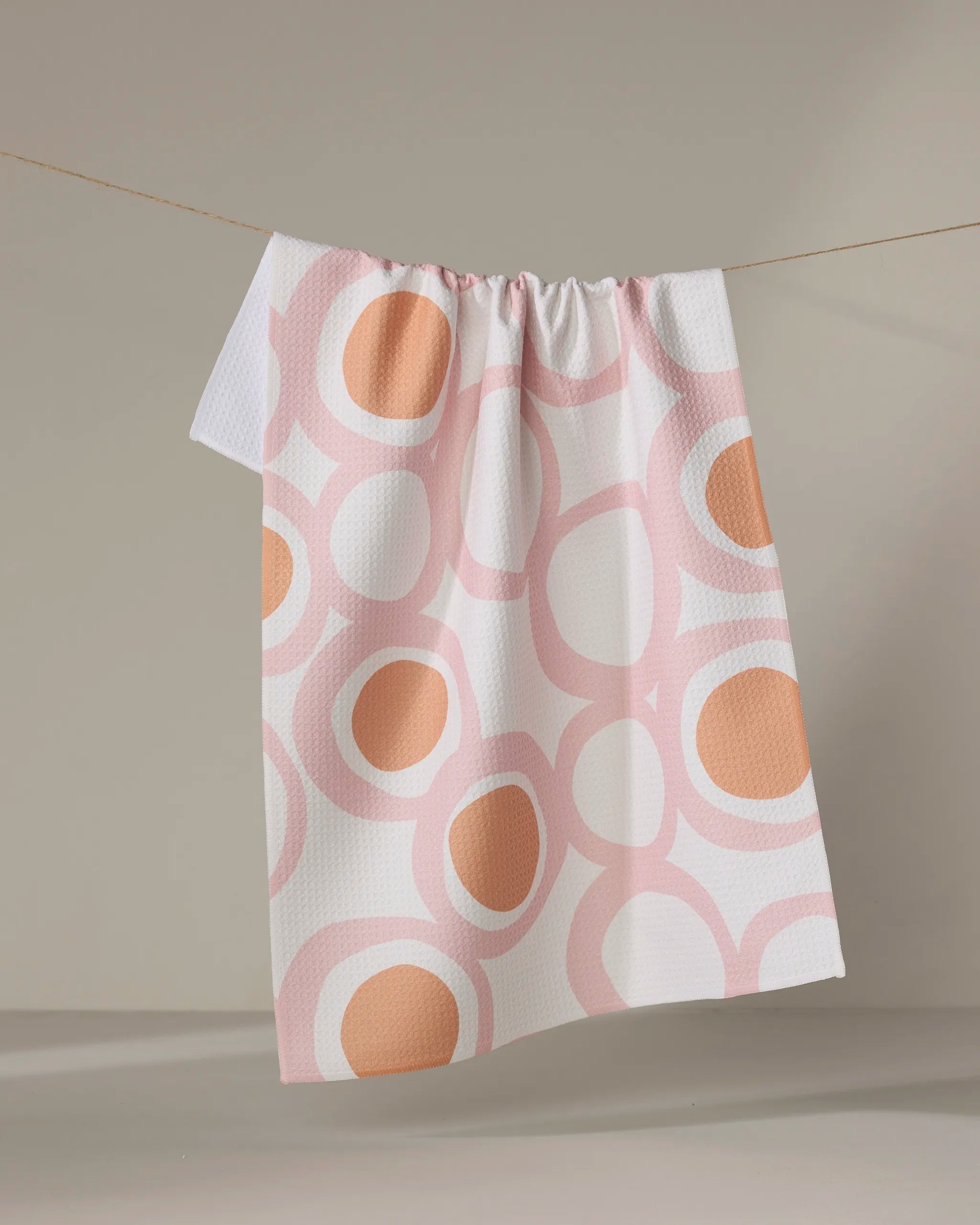 The Bouncing Balls tea towel by Lizzie Clark features a textured white surface with pink and orange circles. Made from ultra-absorbent, recycled materials, it brings eco-friendly flair to your kitchen.