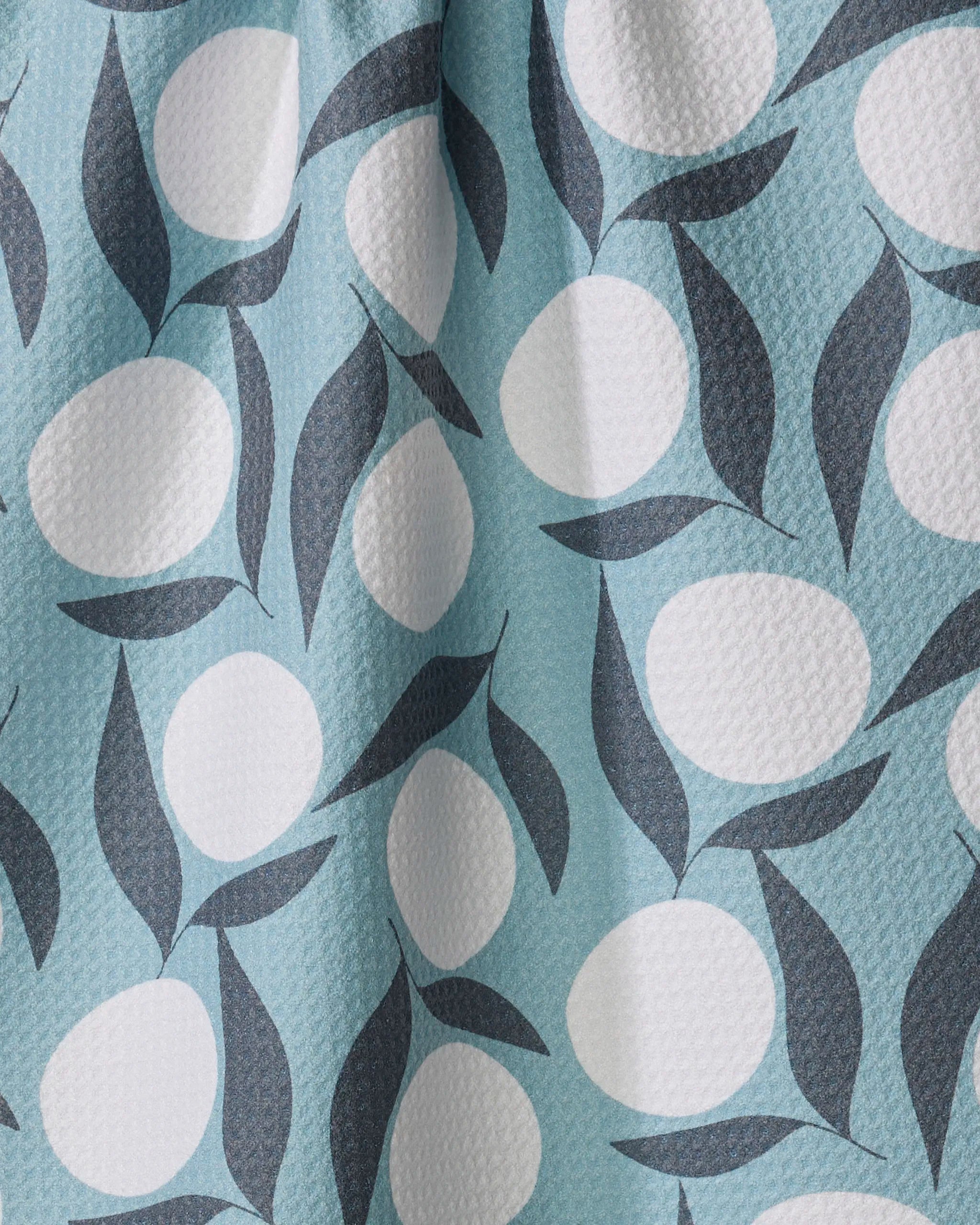 Bouncing Blooms by Lizzie Clark features white ovals and dark blue leaves on a light blue textured background. This softly draping fabric is ideal for tea towels, adding subtle shadows and folds to your kitchen décor.