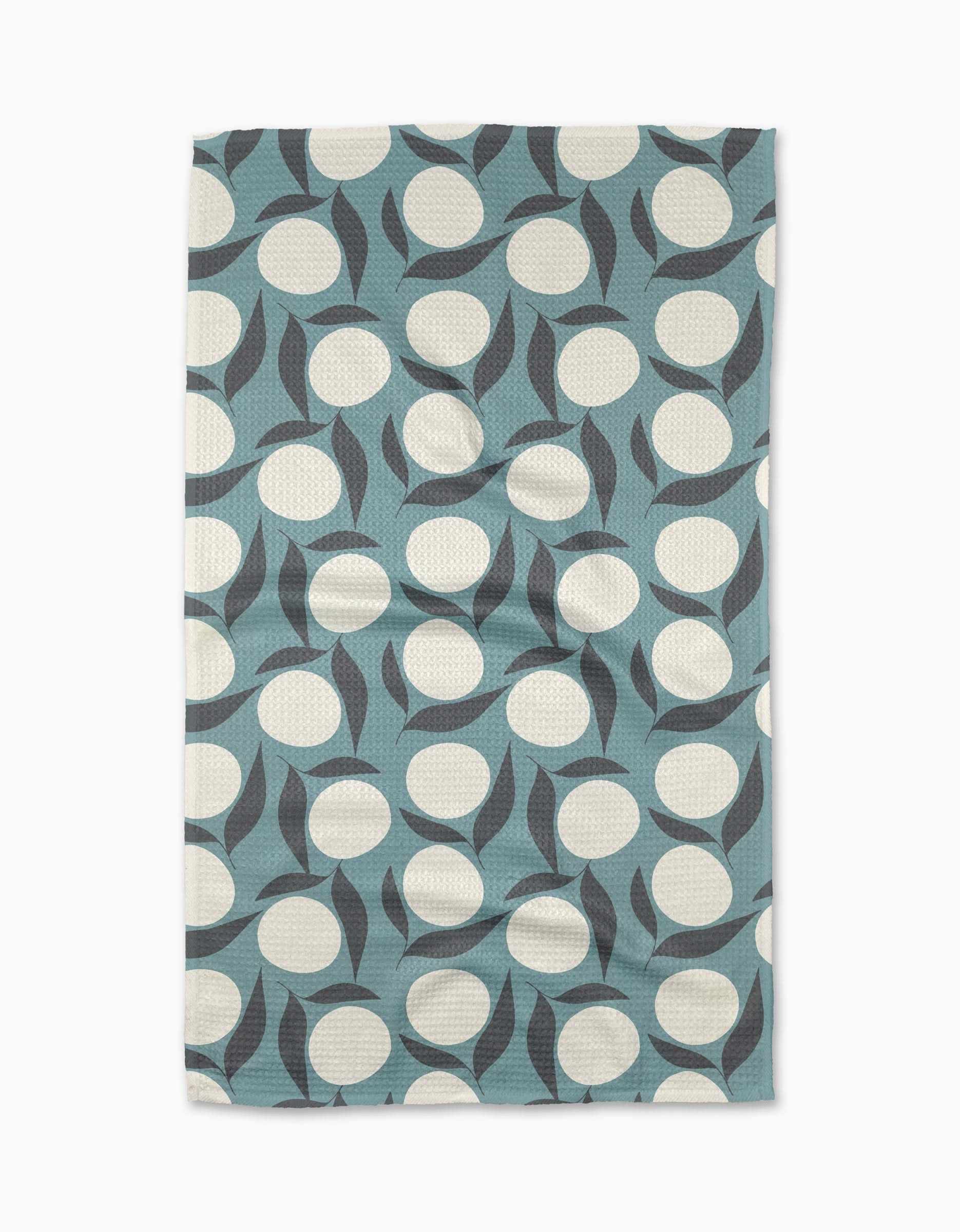 The “Bouncing Blooms” tea towel by Lizzie Clark is a rectangular, blue recycled towel with large white circles and curved black shapes in a modern abstract geometric pattern.