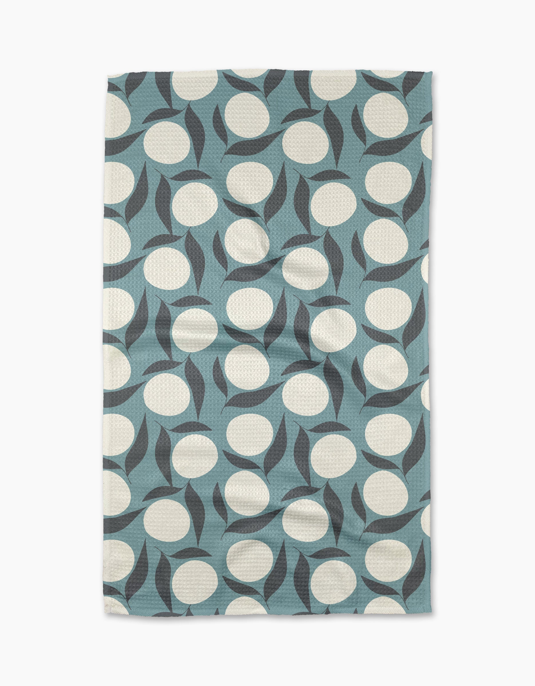 The “Bouncing Blooms” tea towel by Lizzie Clark is a rectangular, blue recycled towel with large white circles and curved black shapes in a modern abstract geometric pattern.