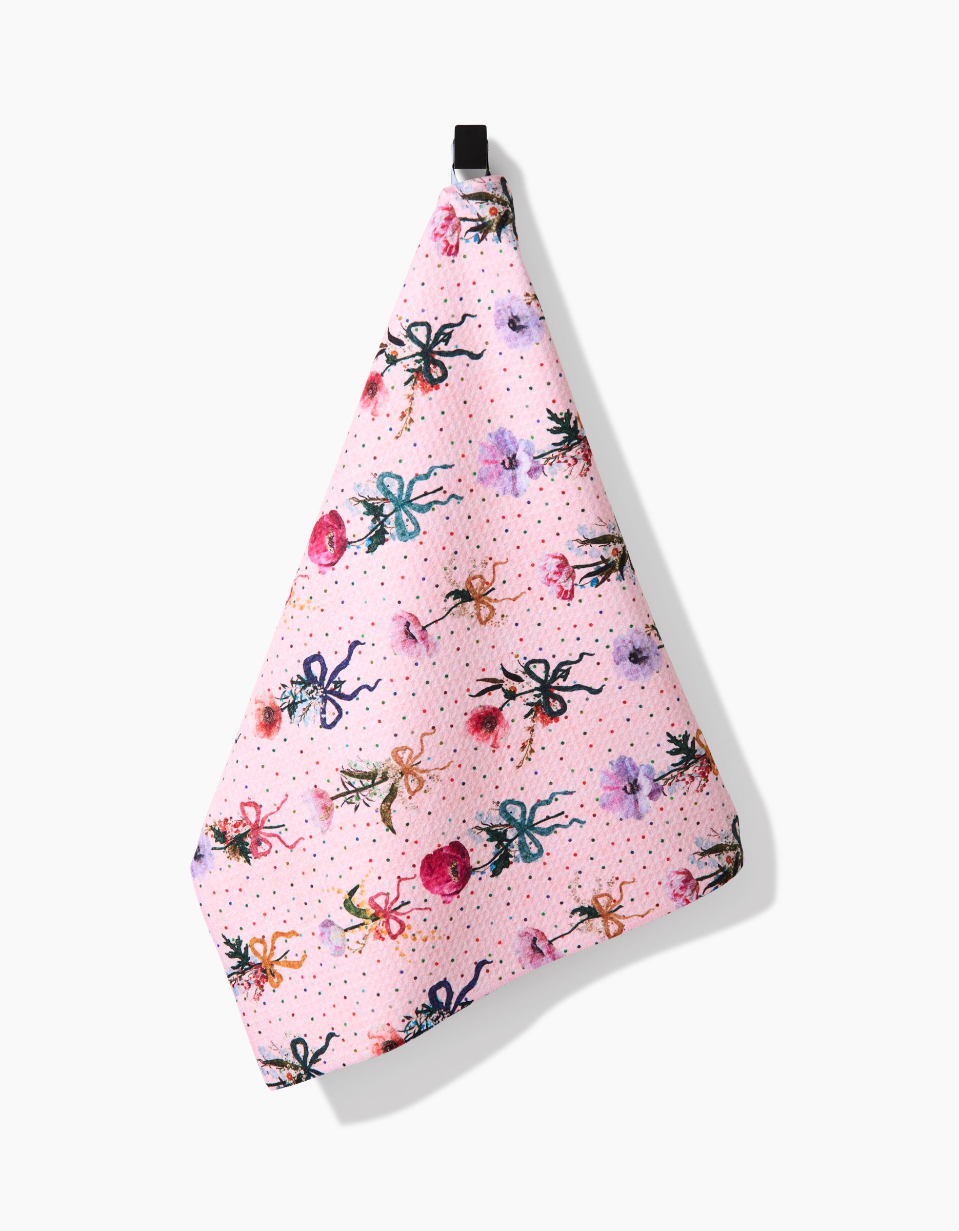 A pink Bows and Dots tea towel by Pascale Dilger, made from recycled materials and decorated with vibrant spiders and flowers, hangs by a black loop against a white background.