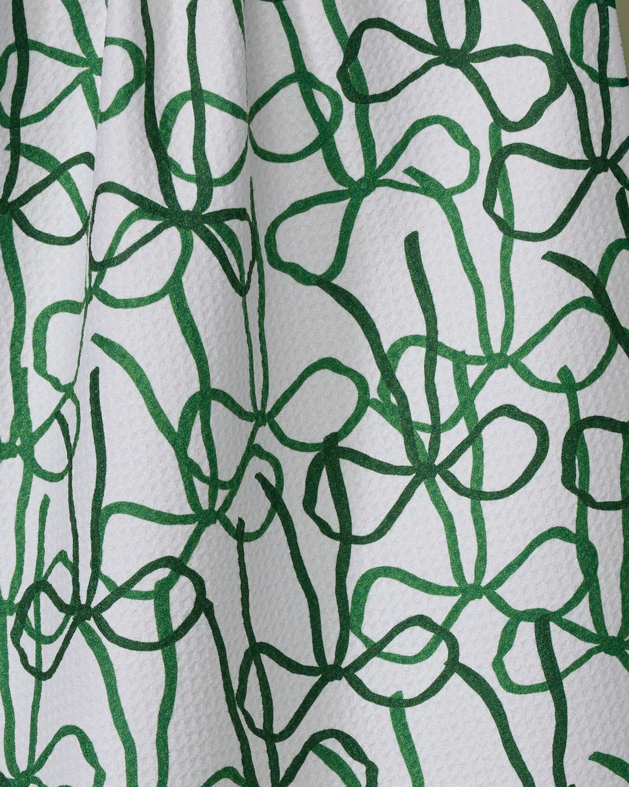 The Geometry Bowtiful kitchen towel features a white, textured surface with an abstract green vine-like pattern, crafted from recycled materials for eco-friendly style.
