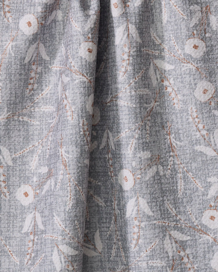 A close-up of the Boyce Grey kitchen towel by Becki Owens, crafted from recycled materials in light gray with a subtle floral pattern of white flowers and beige branches. The softly textured fabric has a gentle, elegant drape.