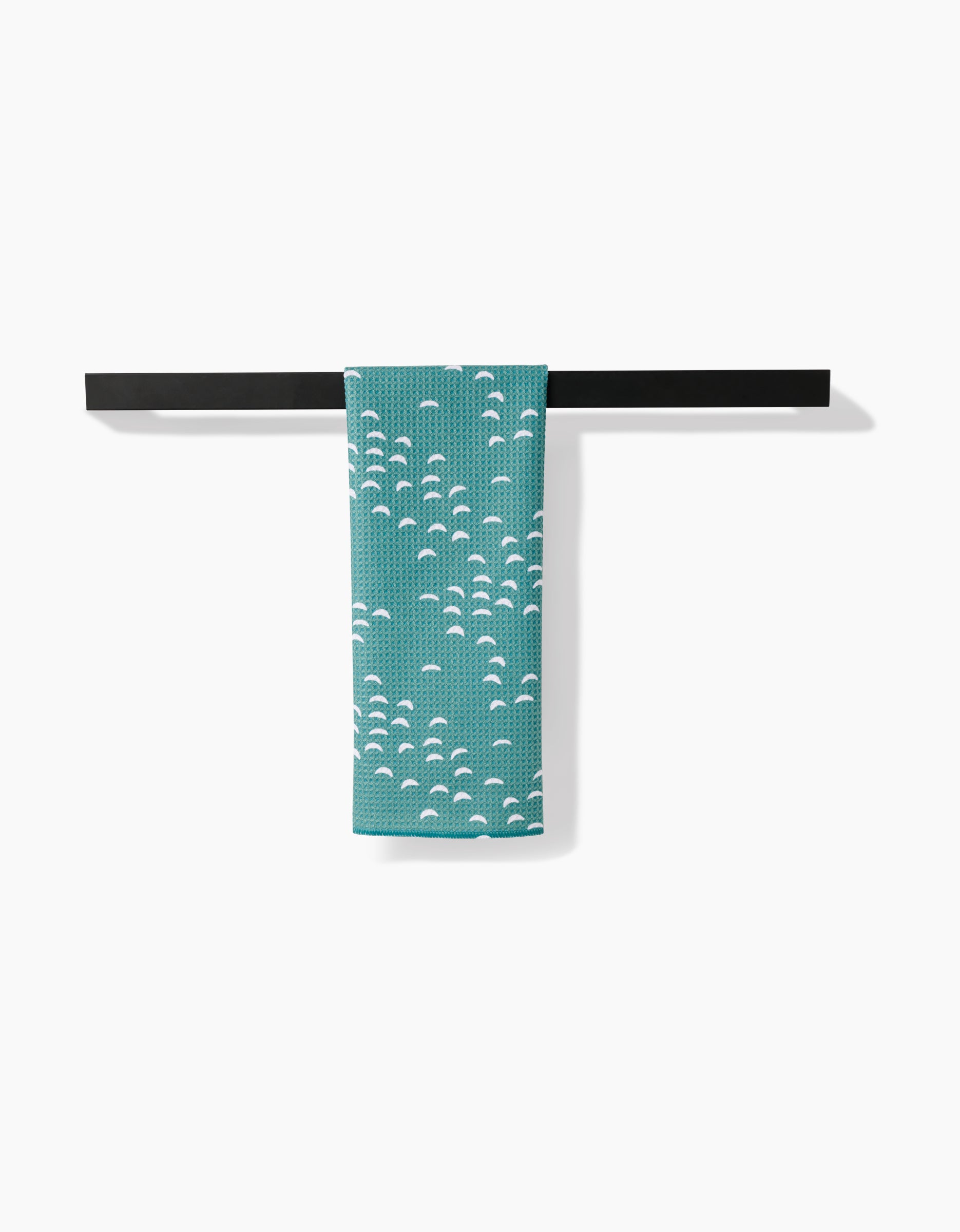 The Jessica Swift Breezeway tea towel, in teal with a white wave pattern, hangs over a slim black bar. Made from ultra-absorbent Geoweave fabric, it combines style and function against a simple white background.