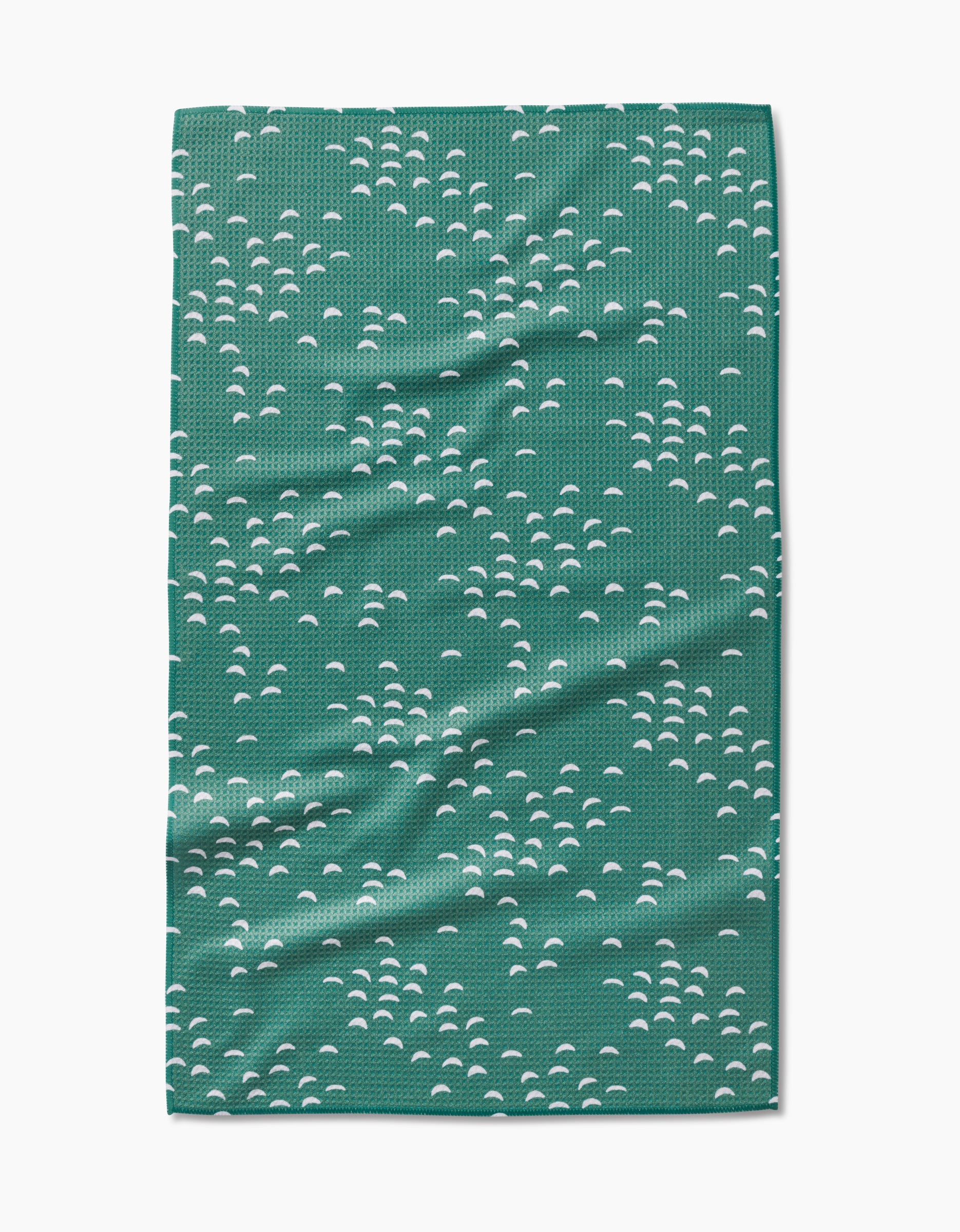The Breezeway tea towel by Jessica Swift features a repeating pattern of small white semi-circular shapes on green, made with ultra-absorbent Geoweave fabric. The towel is shown flat with slight wrinkles visible.