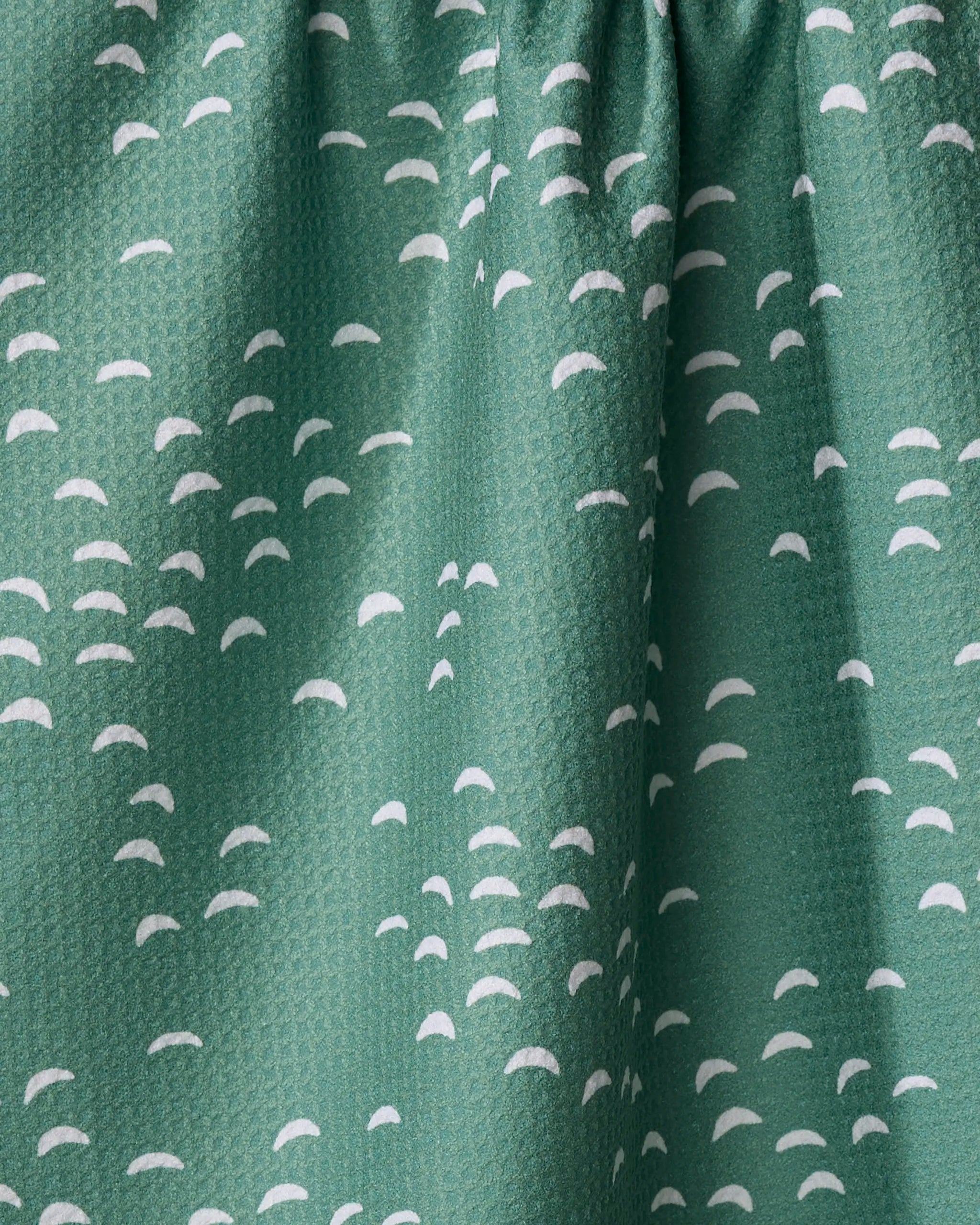 Close-up of Breezeway fabric by Jessica Swift, made from recycled materials, featuring a gathered top and a repeating pattern of small white semi-circles on green.