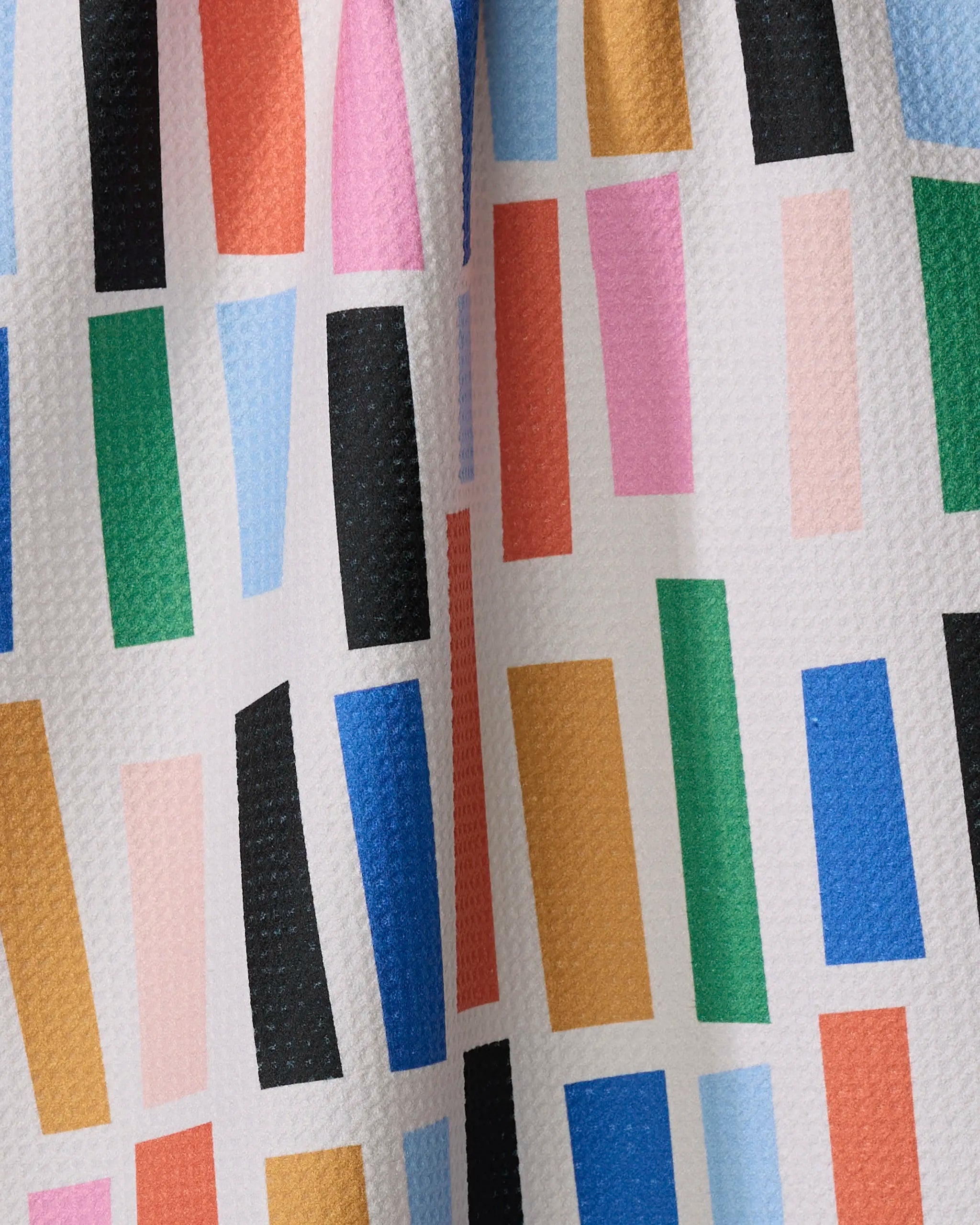 The Bricks tea towel by Jennifer Bouron features vibrant, randomly arranged blue, green, pink, red, orange, and black rectangles on a textured white background, and is crafted from recycled materials.
