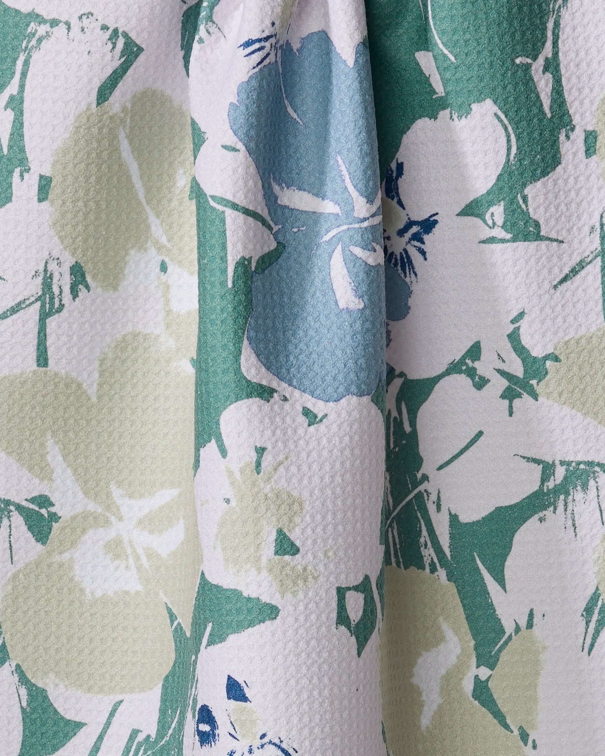 Close-up of Geometry's Brie recycled kitchen towel featuring a textured, slightly bumpy fabric with abstract floral and leaf designs in pastel green, light blue, white, and navy for a charming, painterly look.