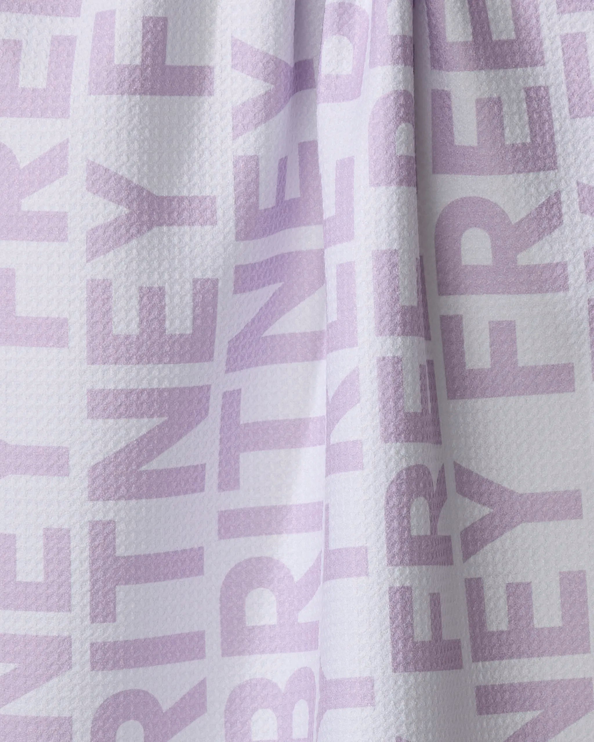A close-up of ultra-absorbent white textured Britney fabric from The Buy Guide, featuring large, light purple "FREE BRITNEY" text in a bold sans-serif font printed repeatedly, possibly designed as a tea towel.