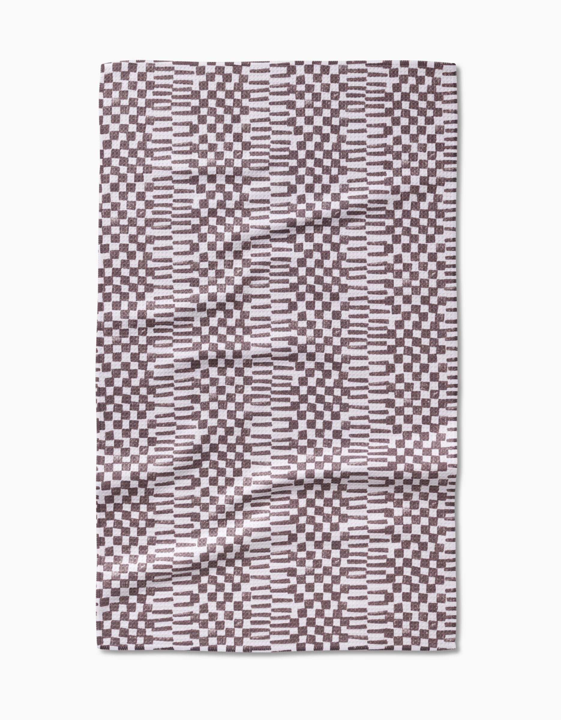 A Chutes Coffee tea towel from Studio Jeannot is shown laid flat on a white background, featuring a geometric pattern of alternating black and white horizontal stripes and small checkerboard squares, crafted from Geoweave fabric.