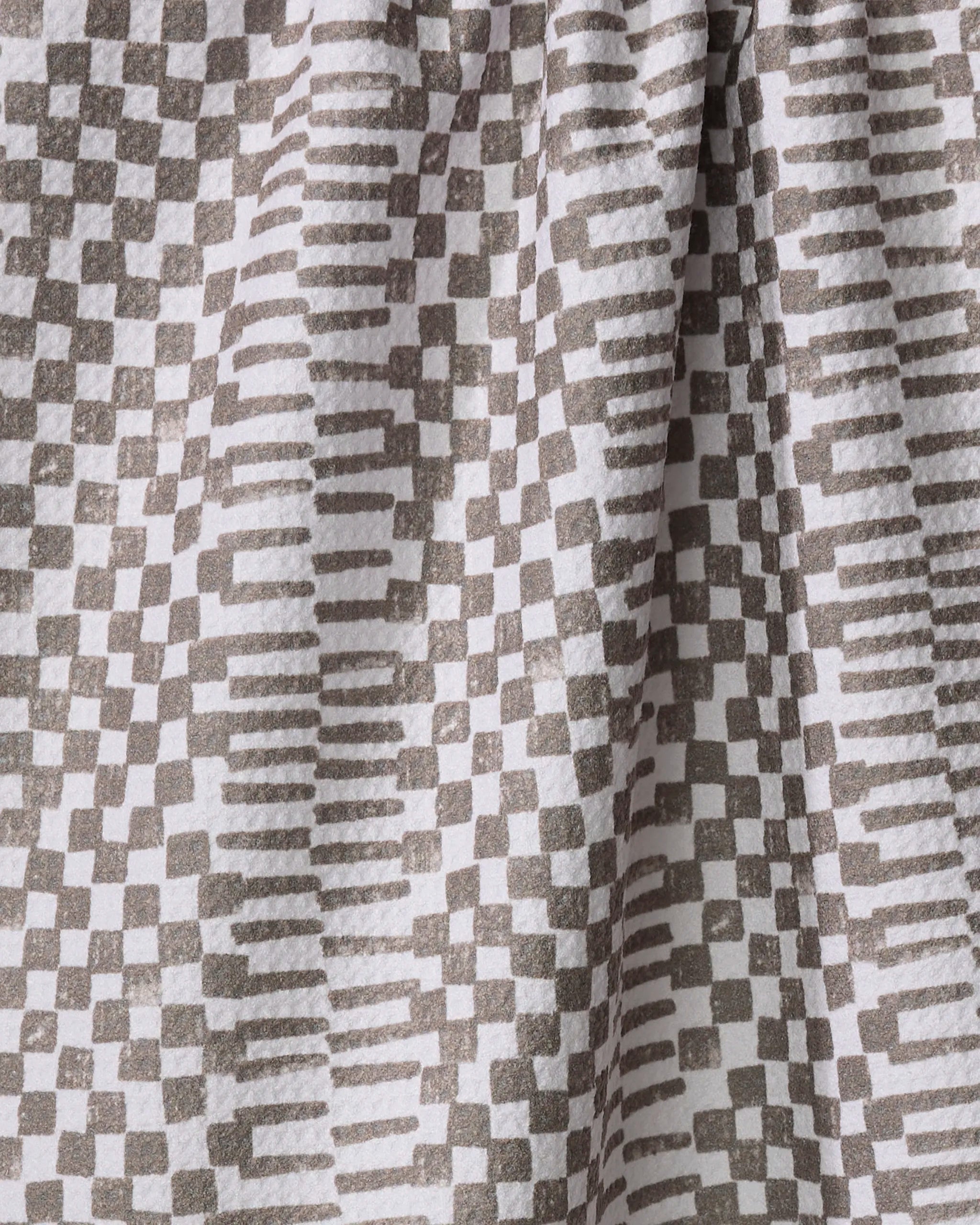 A close-up of Studio Jeannot's Brown Chutes tea towel, featuring an ultra-absorbent fabric with a geometric pattern of gray squares and rectangles on white, shown with folds and soft shadows.