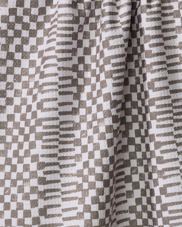 A close-up of Studio Jeannot's Brown Chutes tea towel, featuring an ultra-absorbent fabric with a geometric pattern of gray squares and rectangles on white, shown with folds and soft shadows.