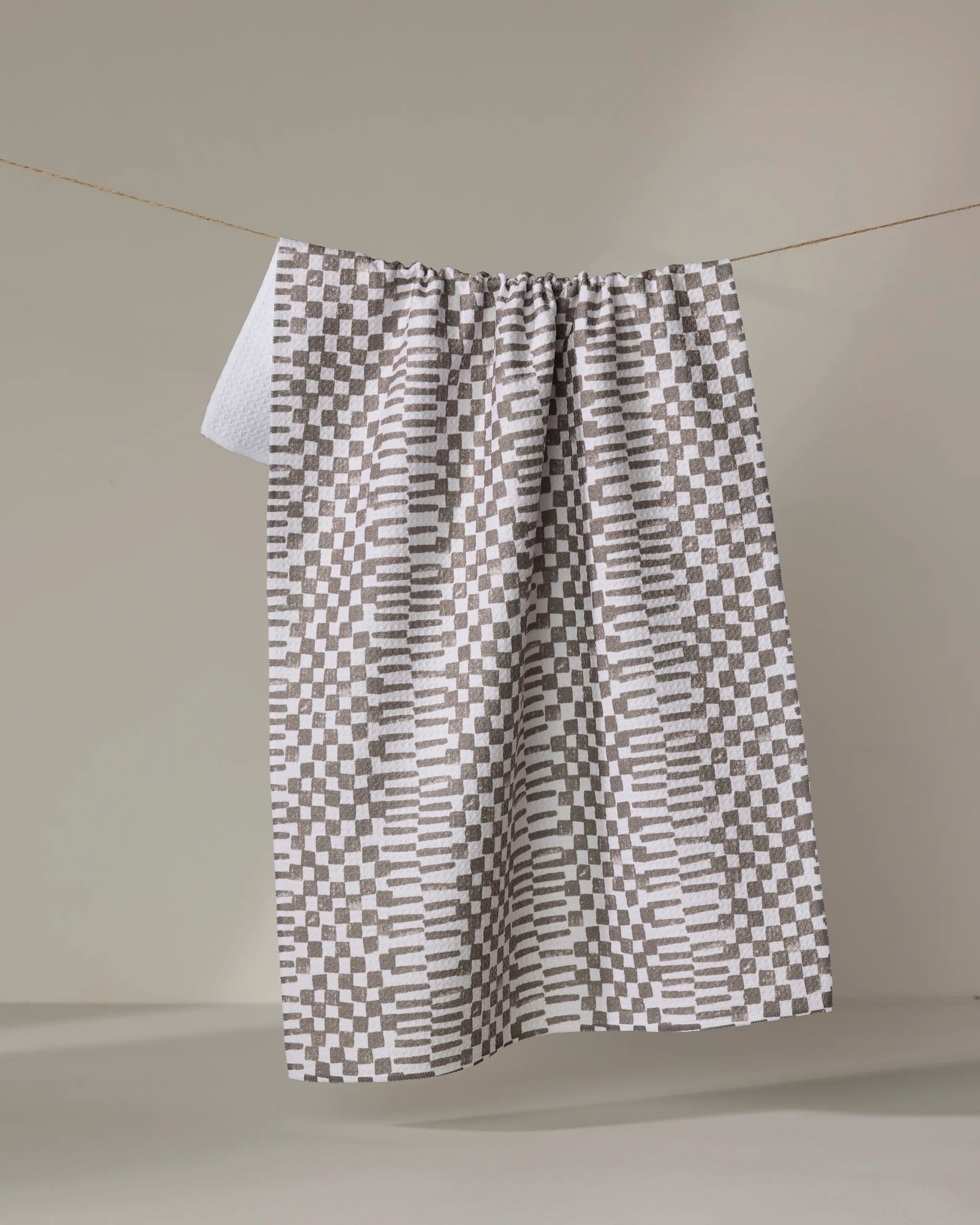 The Brown Chutes tea towel by Studio Jeannot features a geometric checkerboard pattern in gray and white. Made from ultra-absorbent recycled materials, it offers both style and sustainability for your home.