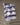 The Geometry Brushline Navy quick-drying tea towel, featuring dark blue and white wavy stripes, hangs on a string above a glass bottle with a wooden cap and two matching textured glasses against a plain backdrop.