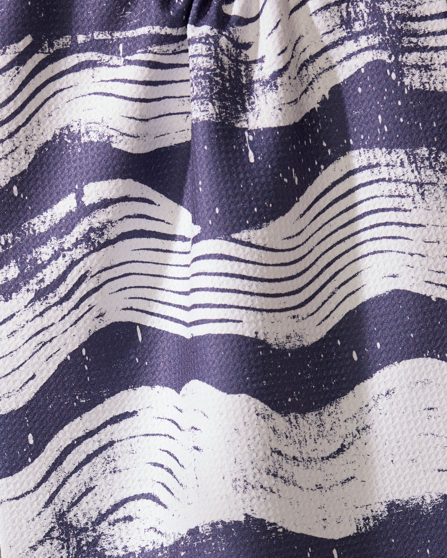A close-up of Geometrys Brushline Navy tea towel, featuring quick-drying fabric and wavy, hand-drawn white stripes on a dark blue background for a dynamic, artistic texture.