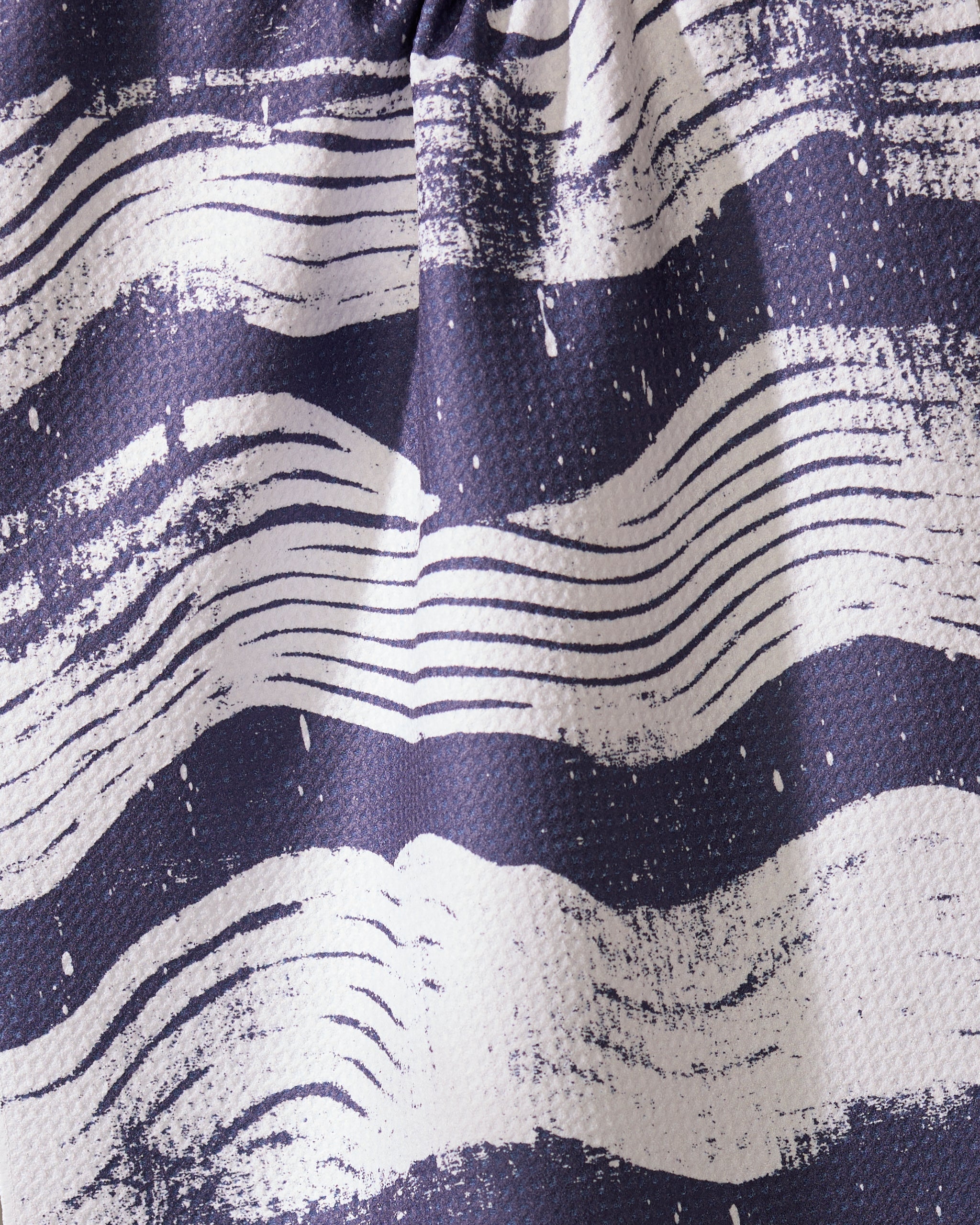A close-up of Geometrys Brushline Navy tea towel, featuring quick-drying fabric and wavy, hand-drawn white stripes on a dark blue background for a dynamic, artistic texture.