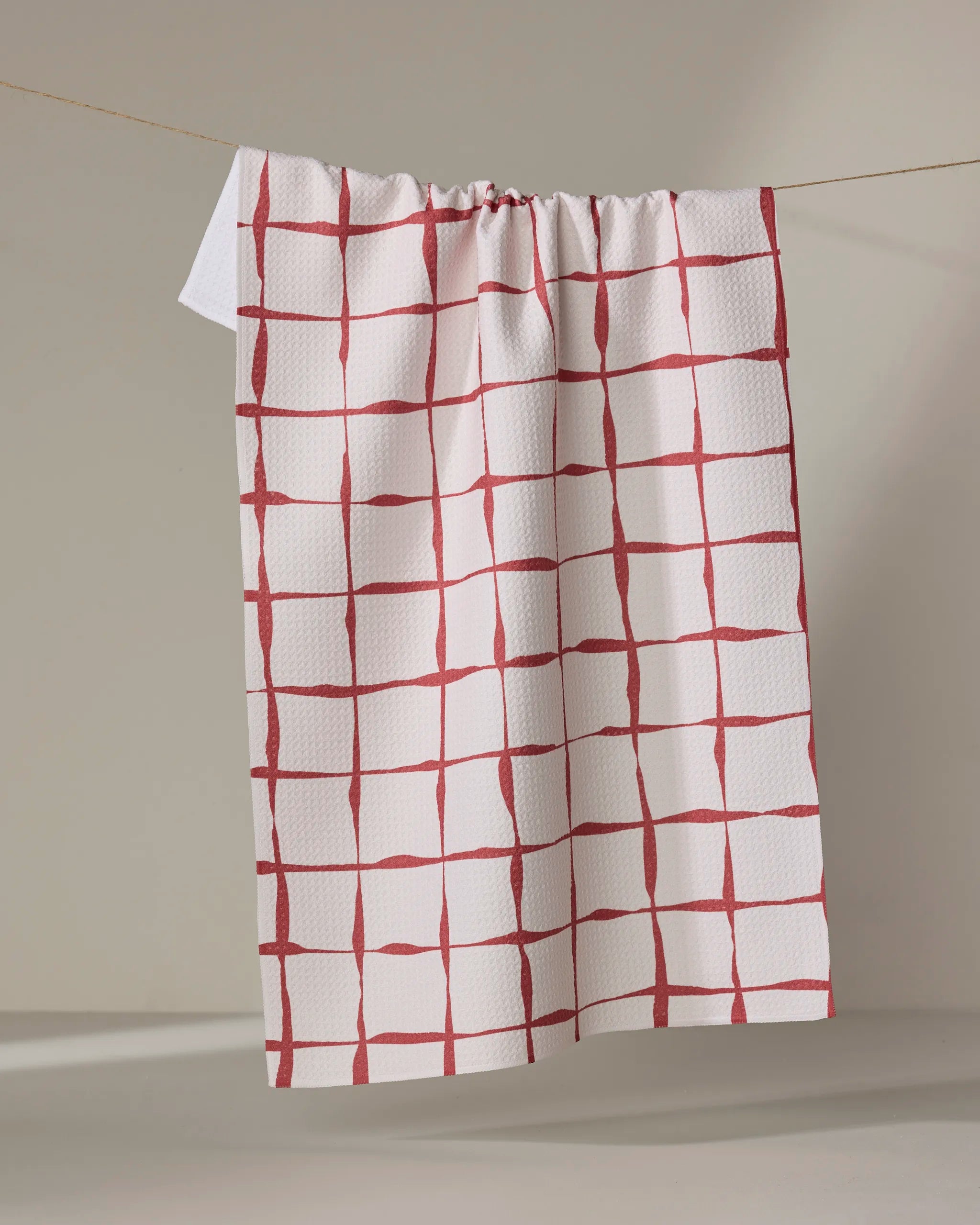 The Brushstroke Checks tea towel by Linda Fox features a red, hand-painted grid on white. Made from recycled materials, this ultra-absorbent and eco-friendly towel adds stylish charm to any kitchen.