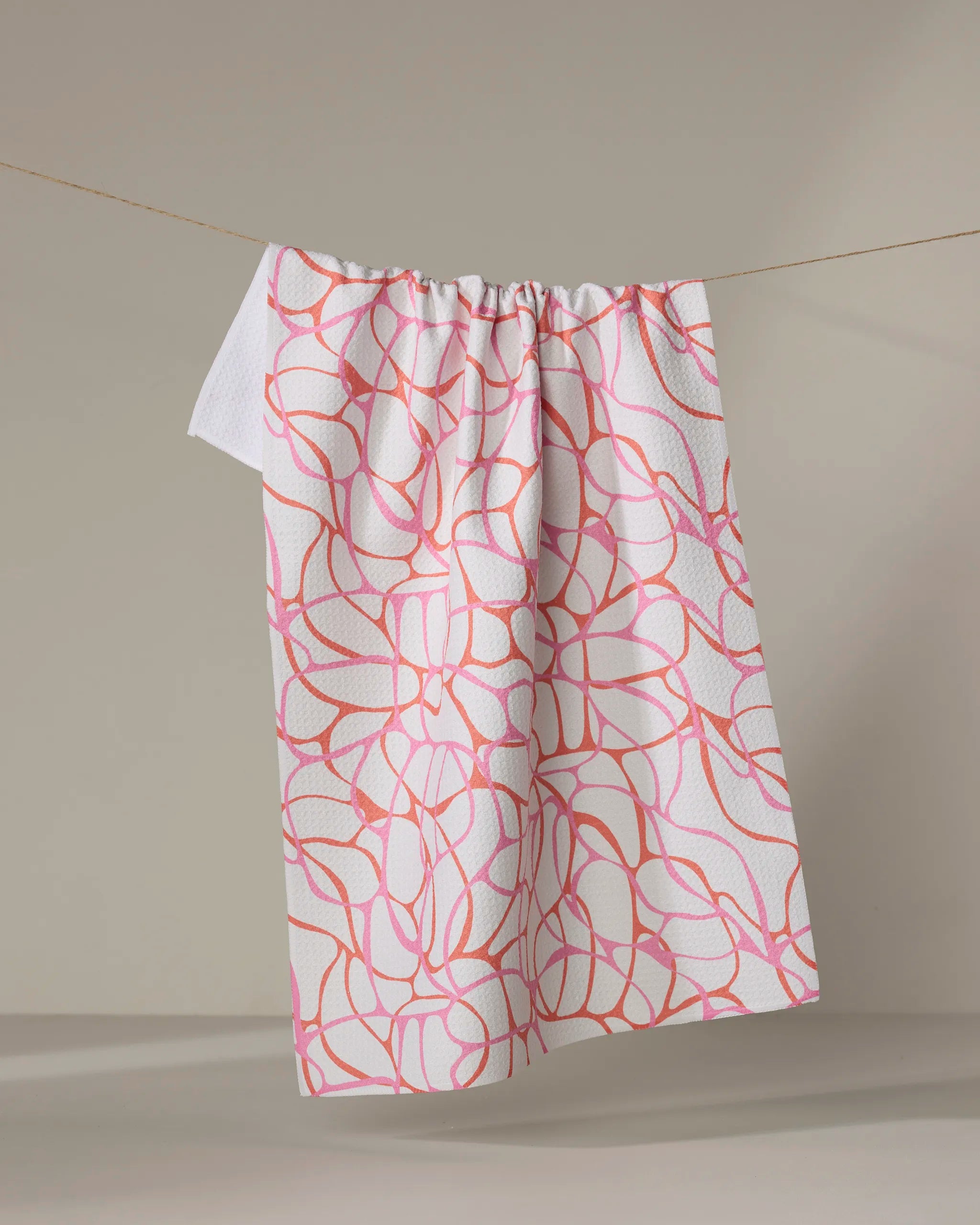 The Bubble Abstract towel by Rachel Parker, featuring a pink and orange abstract line pattern, hangs neatly on a clothesline against a neutral background.