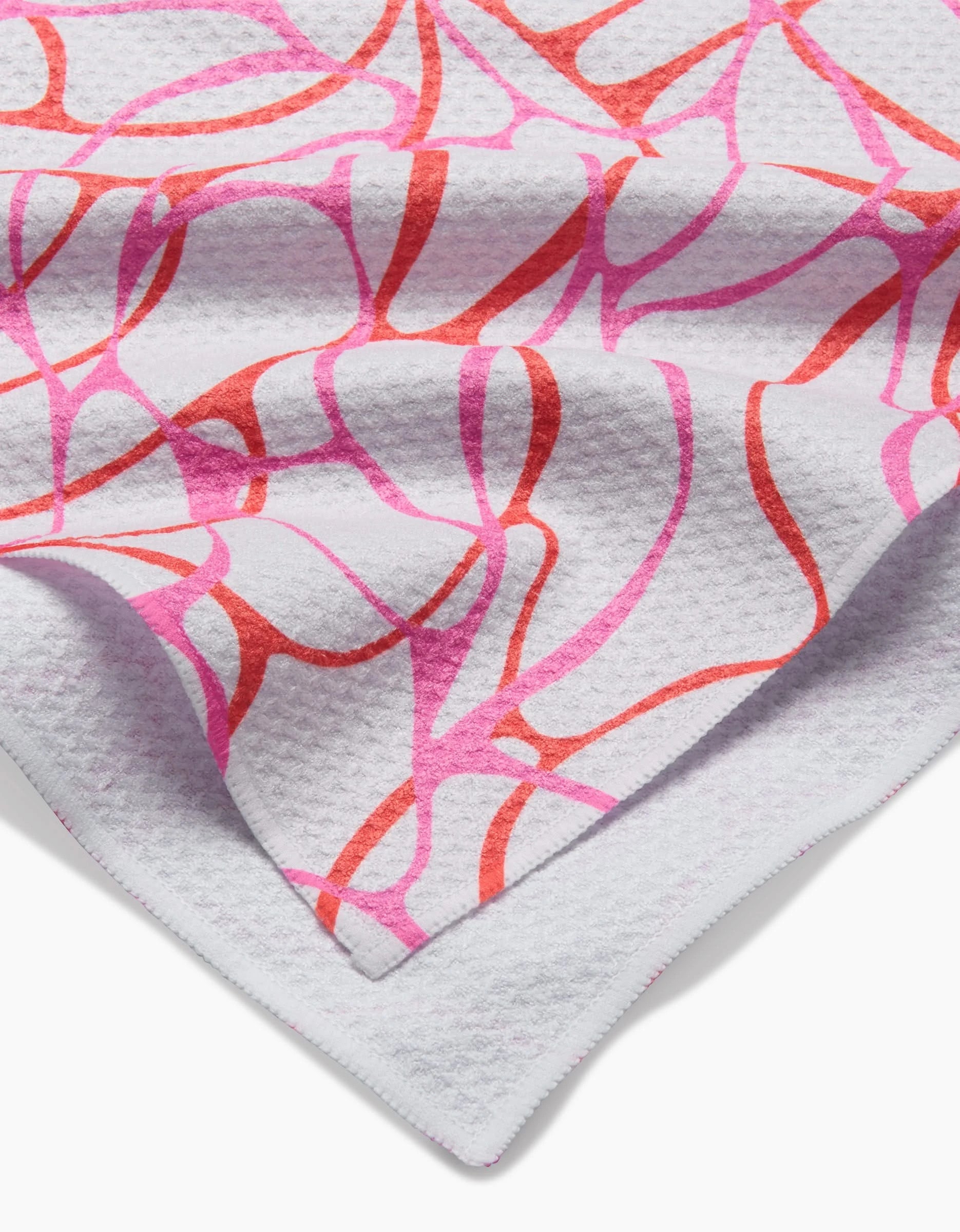 A close-up of the white Geoweave Bubble Abstract tea towel by Rachel Parker displays overlapping pink and red abstract lines. The towel is neatly folded to show both its front design and finished edge.