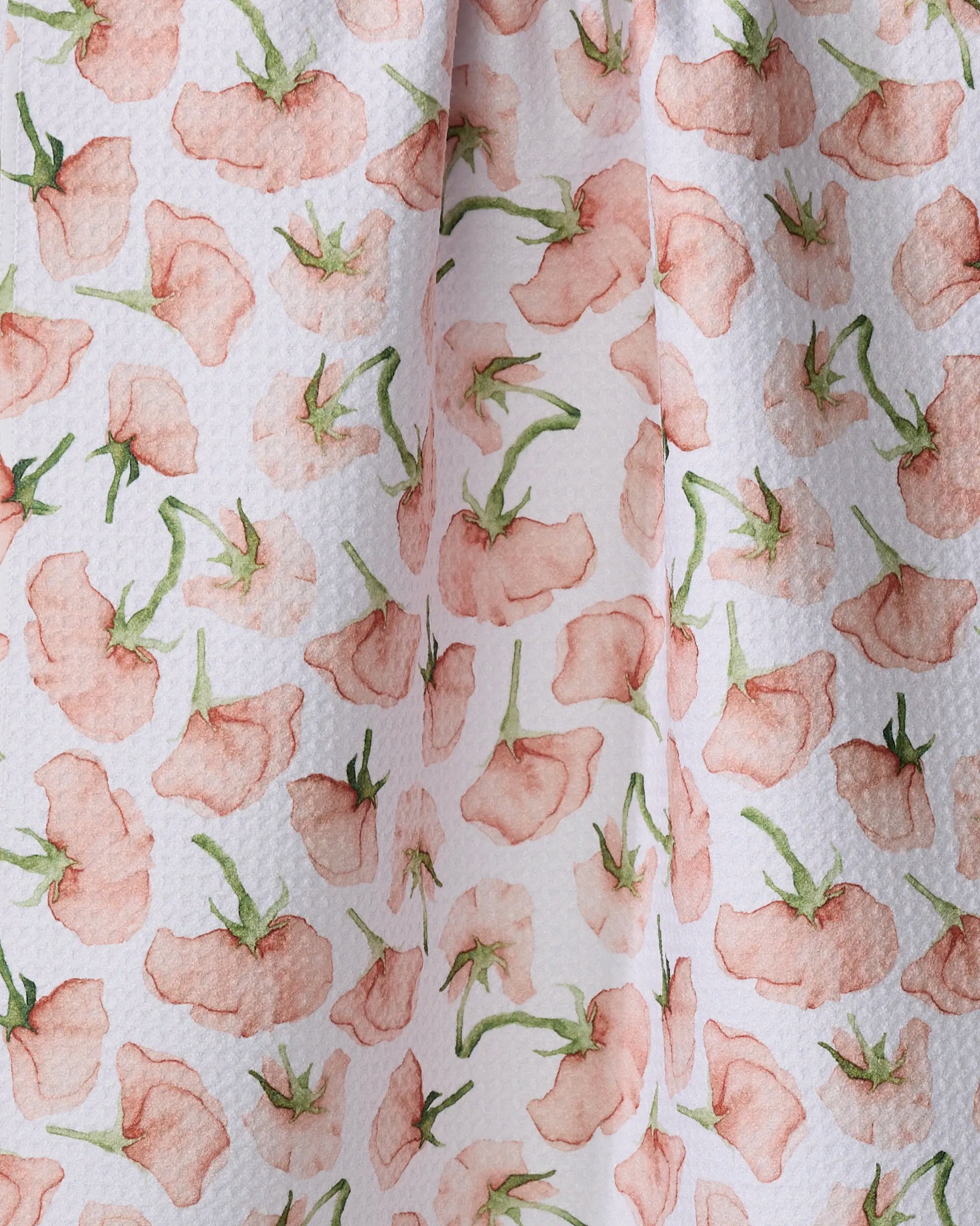 A close-up of Aubrey Fairchild's "Budding Romance" eco-friendly tea towel, softly draped, features a textured, absorbent surface with a watercolor-style pink flower and green stem design on a white background.