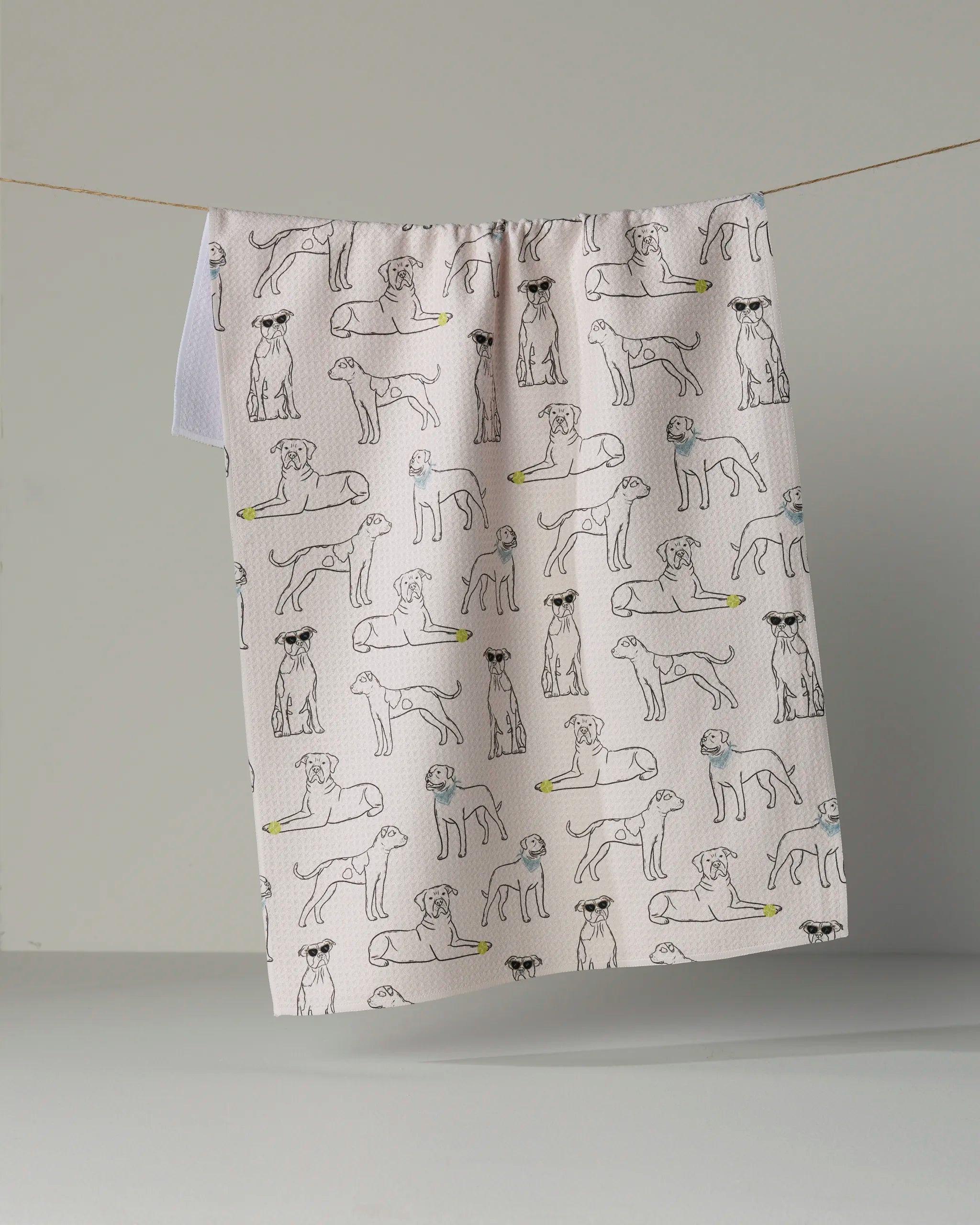 The “Bulldog Buddies” tea towel by Geometry features a beige background adorned with simply outlined bulldogs in playful poses, displayed hanging from a string against a light grey backdrop. This absorbent dish towel brings both charm and practicality to your kitchen décor.