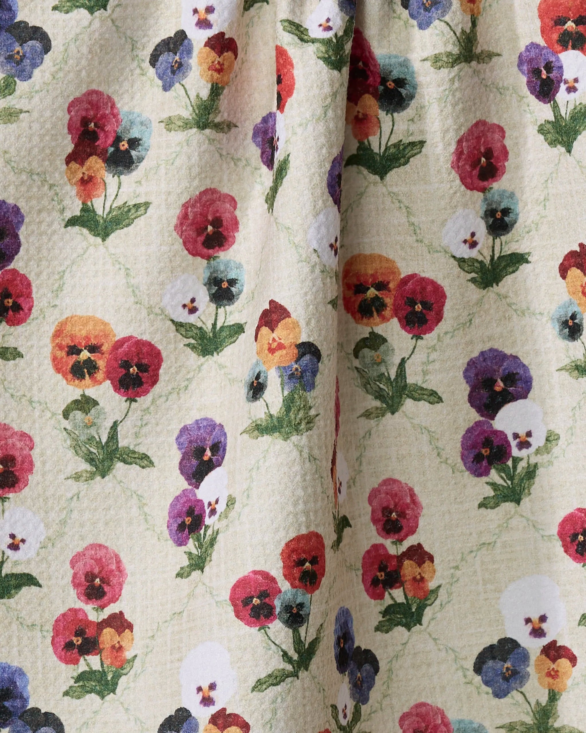 Close-up of Pascale Dilger's eco-friendly "Bunch of Pansies" towel, featuring a textured beige surface with colorful pansy flowers in red, yellow, purple, blue, and green leaves.