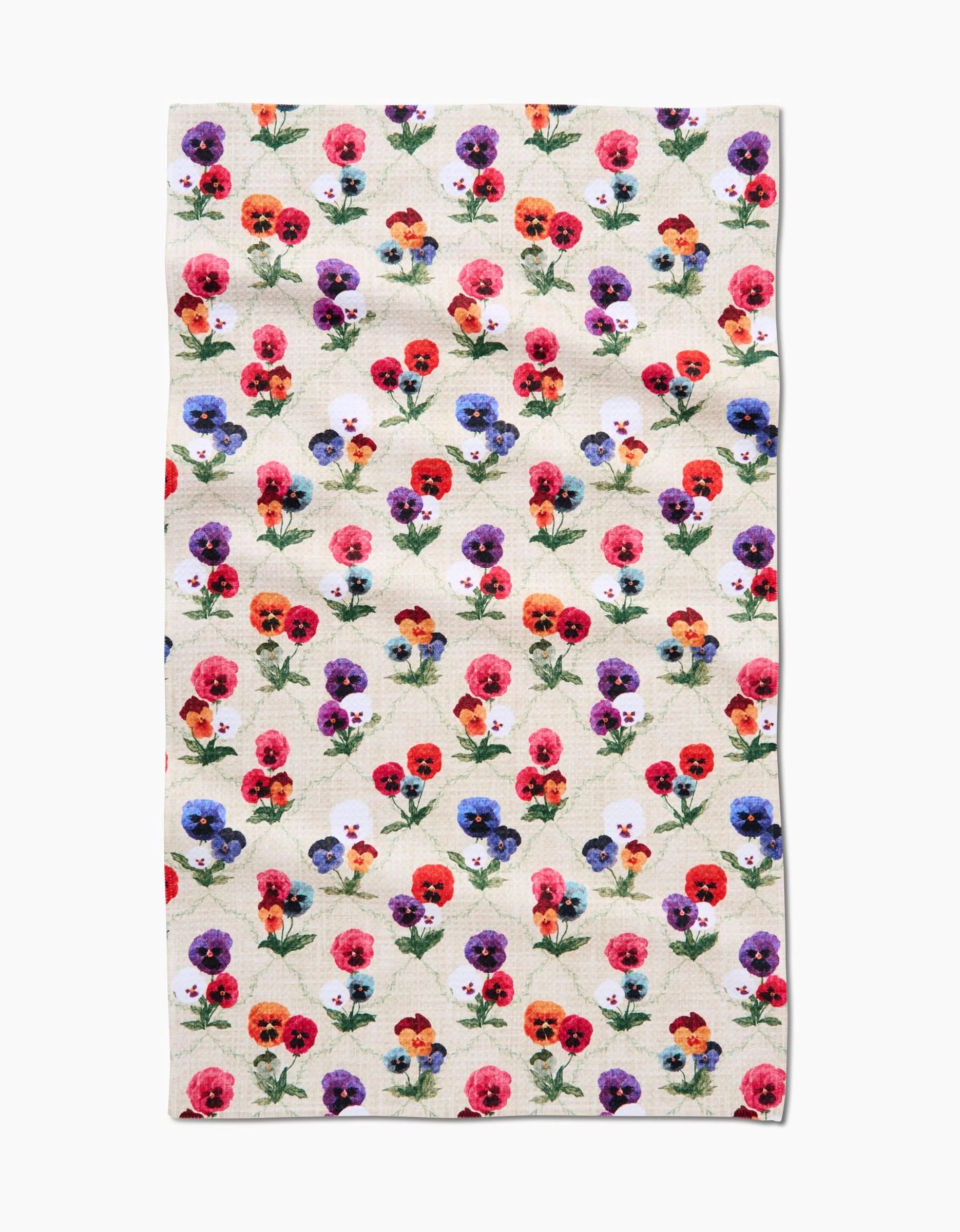The Bunch of Pansies tea towel by Pascale Dilger features a rectangular beige Geoweave fabric with a vibrant pansy flower pattern in red, pink, purple, yellow, and orange, accented by green stems and leaves.