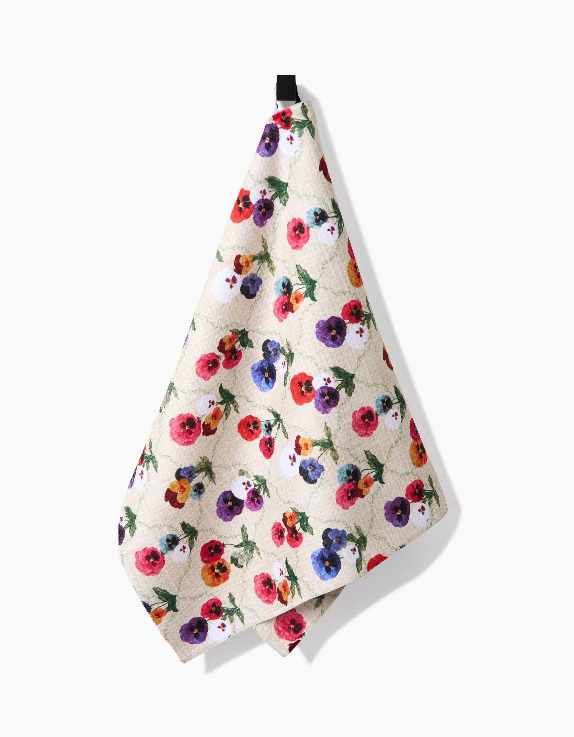 The Pascale Dilger Bunch of Pansies tea towel features a vibrant red, purple, yellow, and pink pansy design on white Geoweave fabric, offering superior absorbency. Shown hanging from a black loop against a plain white background.