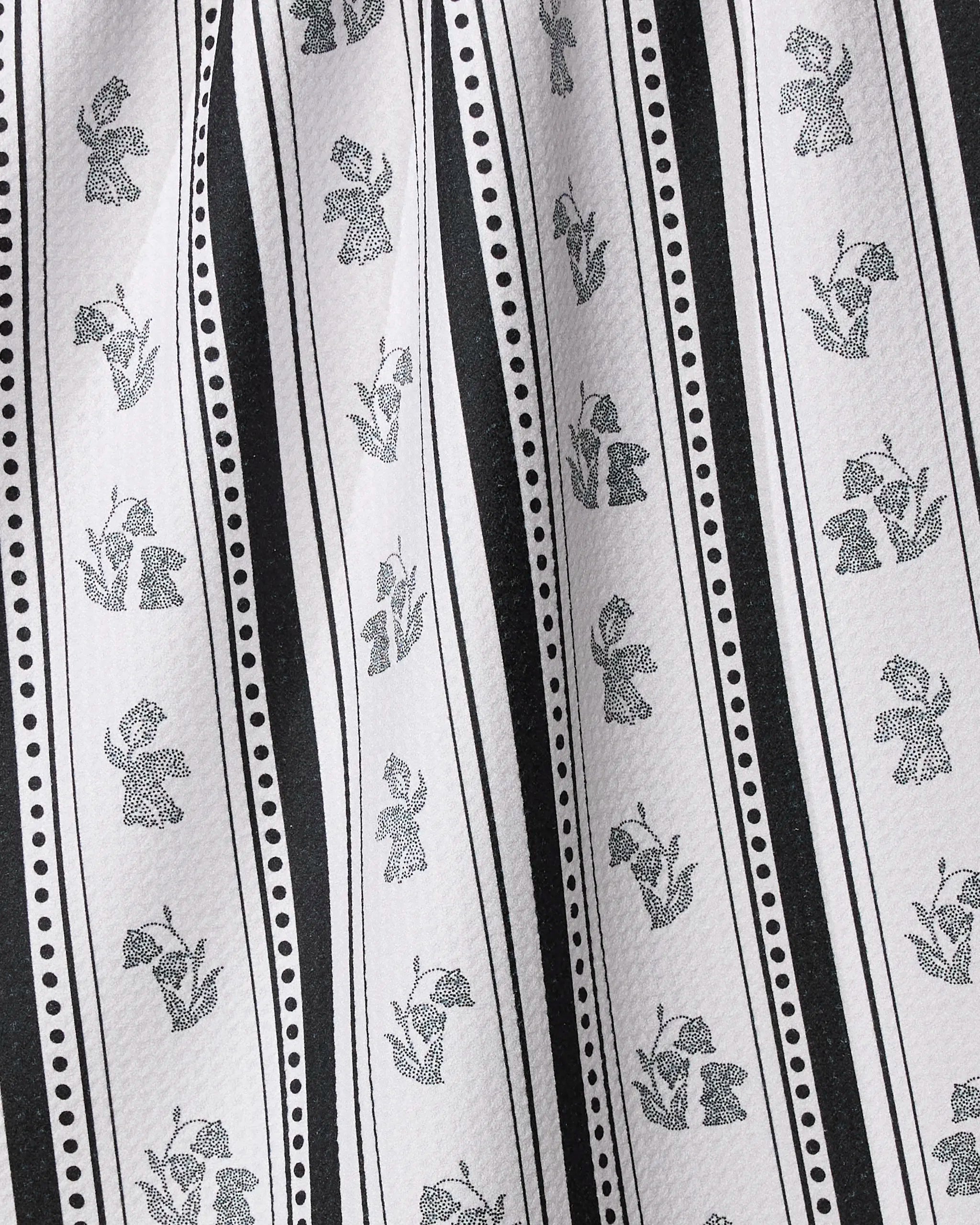 Geometry’s Bunny Dots Stripe kitchen towel features black and white vertical stripes with alternating small flower and tulip patterns, separated by dotted and solid lines. Made from recycled materials, it has a soft texture and gentle folds.