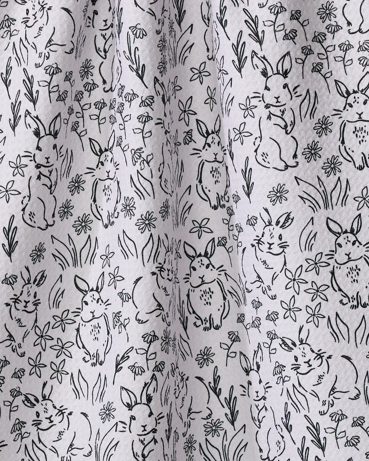 The Bunny Rabbit Garden tea towel from Charlie Rowan Designs features black line drawings of rabbits and flowers on light gray recycled fabric, combining eco-friendly materials with a charming, stylish design for your kitchen.