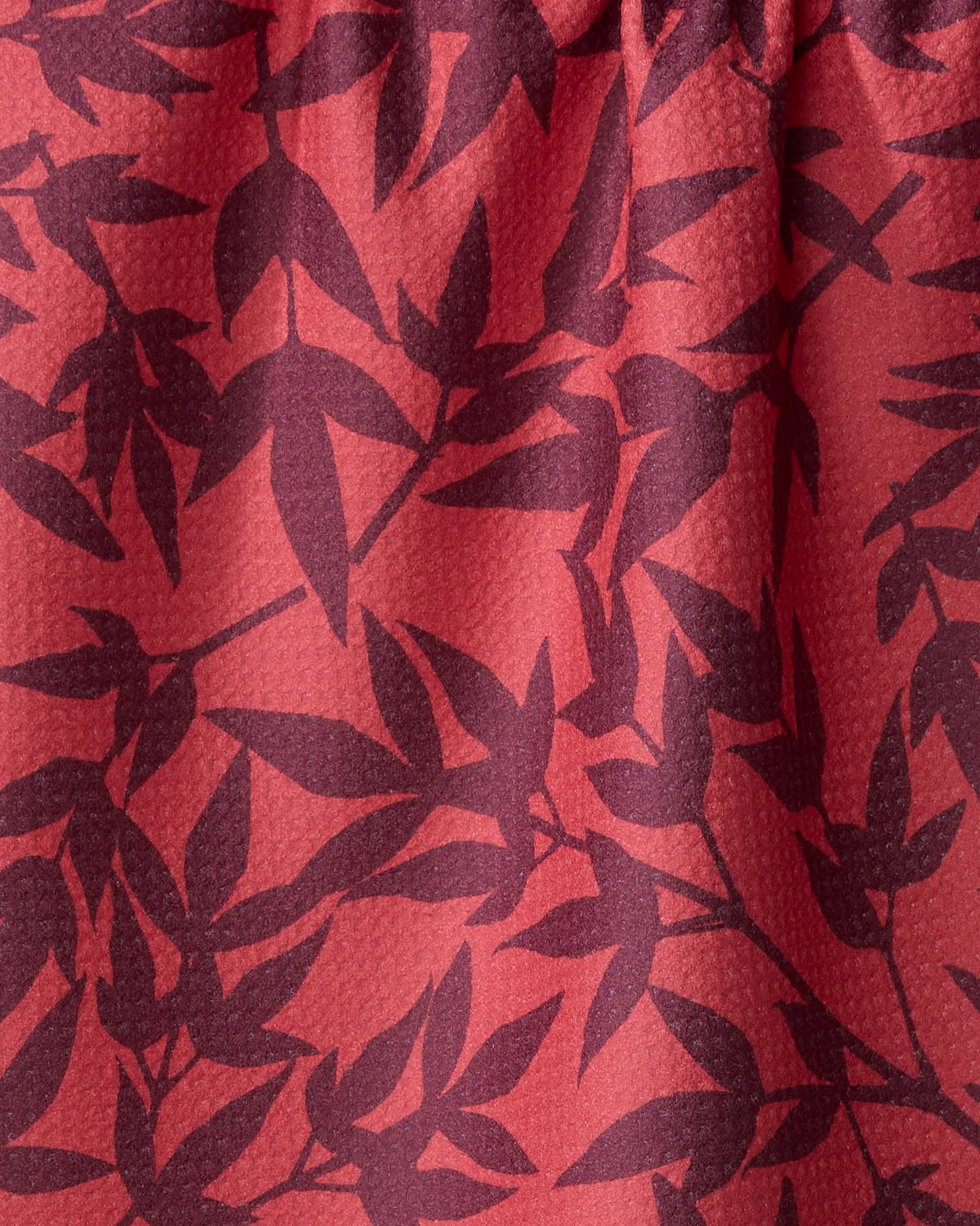 Close-up of the ultra-absorbent Burgundy Branches tea towel by Rebecca Bobko, showcasing a red textured fabric with dark purple leafy branch patterns.