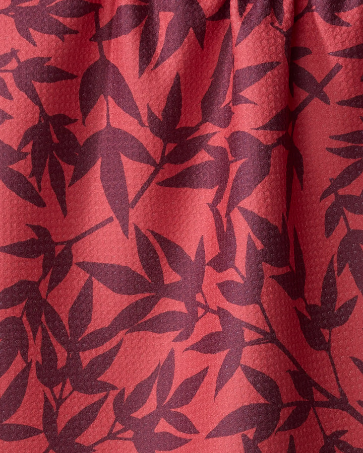 Close-up of the ultra-absorbent Burgundy Branches tea towel by Rebecca Bobko, showcasing a red textured fabric with dark purple leafy branch patterns.