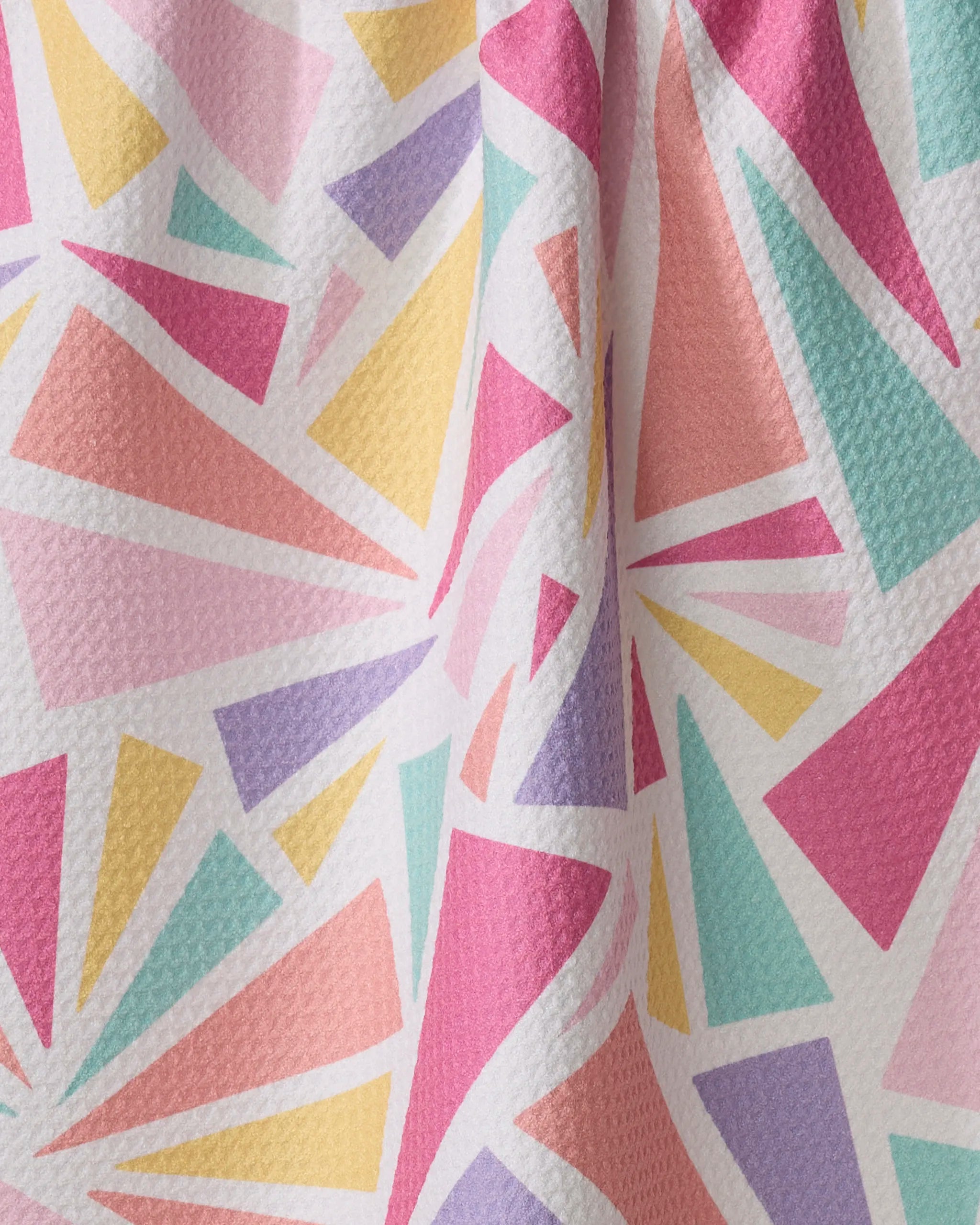 Burst by Rebecca Bobko is a white textured kitchen tea towel made from recycled materials, featuring a vibrant geometric design with overlapping triangles and shapes in pink, yellow, orange, purple, and teal.