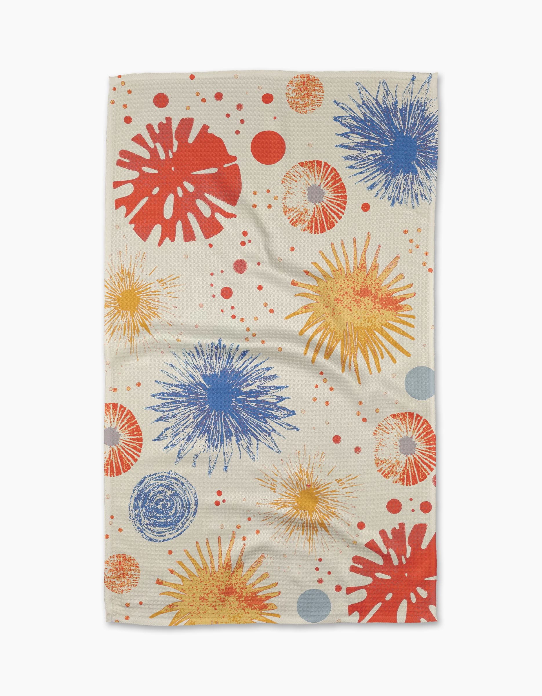 The Geometry Bursting Skies White tea towel features a playful Geoweave™ pattern of abstract starburst shapes and scattered dots in red, yellow, and blue on beige, blending modern style with vibrant color.