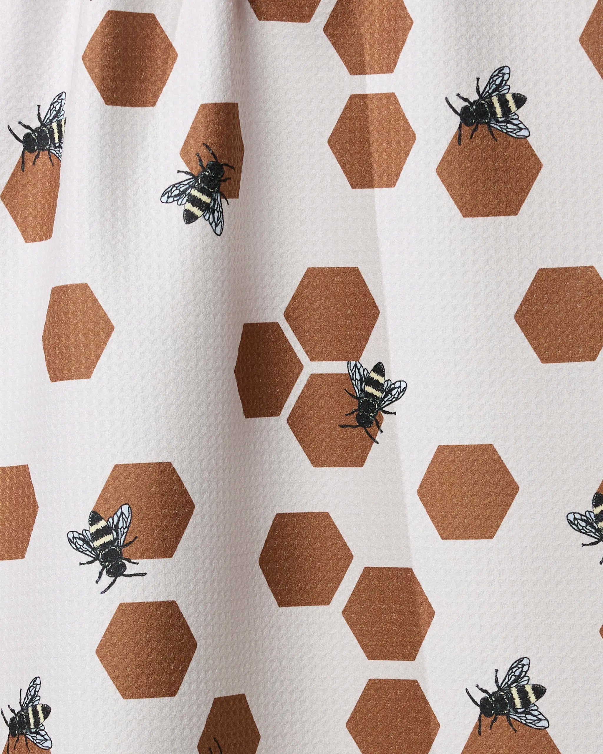 The Geometry "Busy Buzzin" tea towel features brown honeycomb-like hexagons and black-and-yellow bees on a white textured background, designed for quick drying.