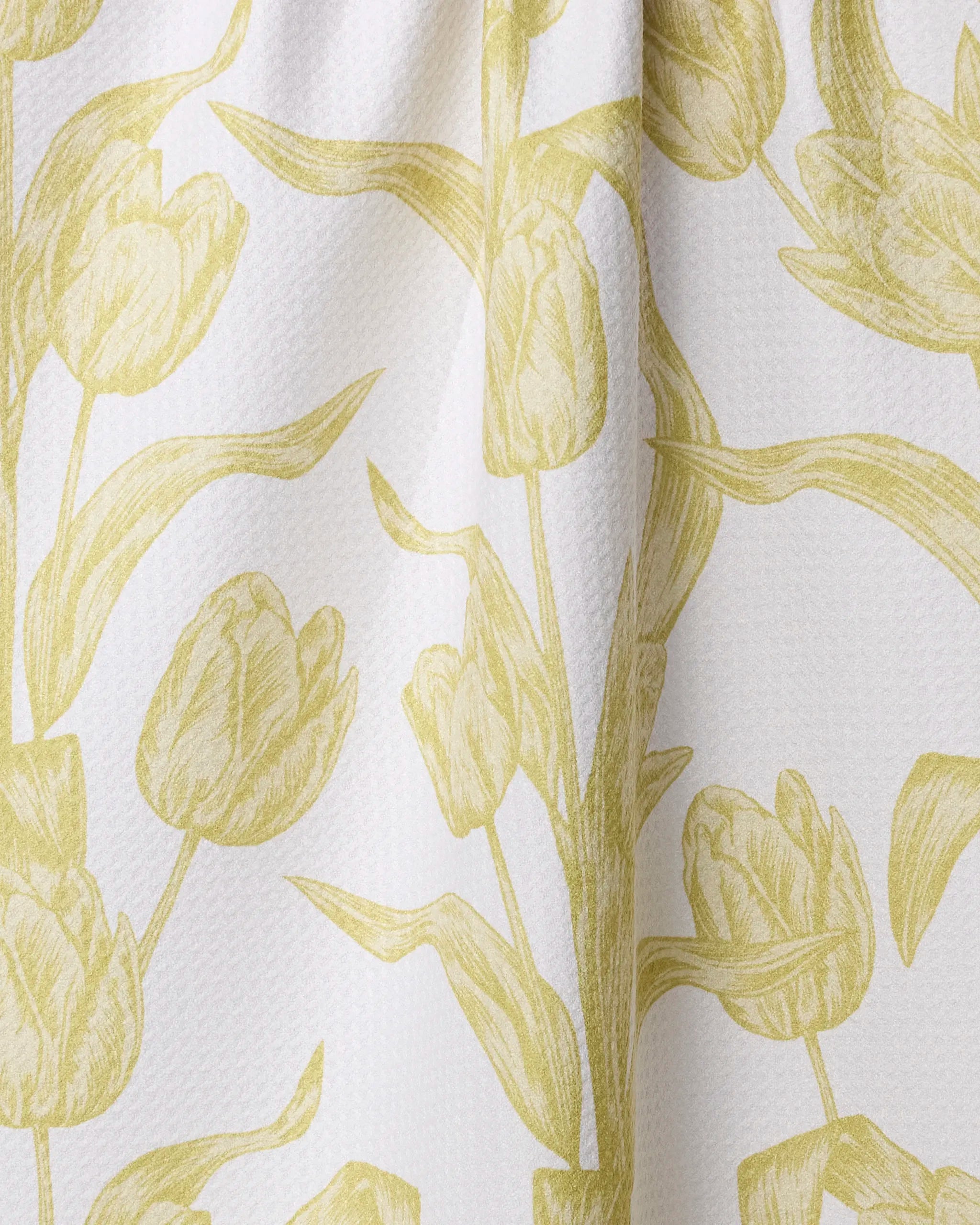 The Geometry Butter Tulips tea towel is white and quick-drying, featuring a textured surface and a cheerful repeating yellow tulip floral pattern with stems, leaves, and blossoms.